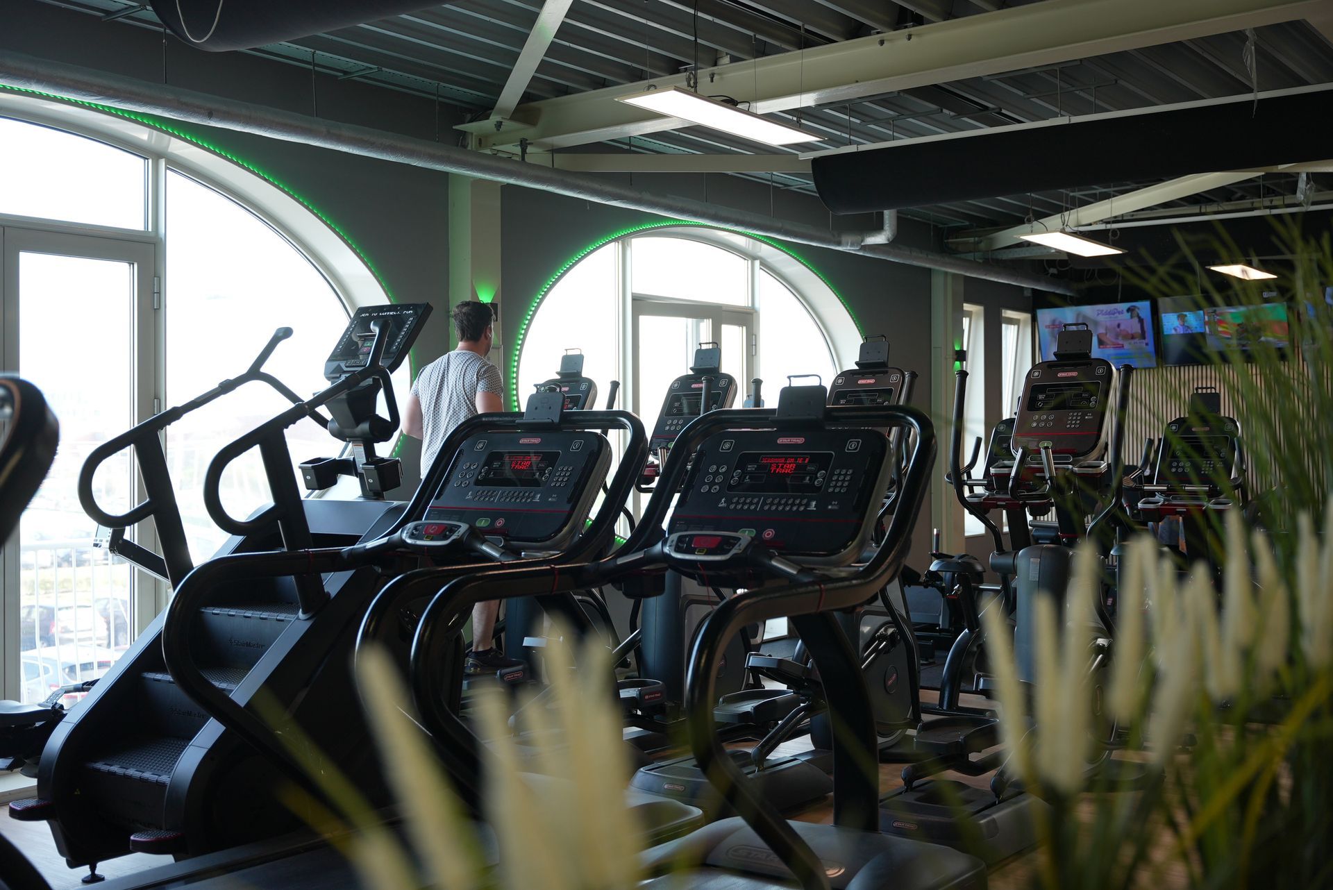Interieur van een sportschool met diverse fitnessapparaten en een persoon die een zittend apparaat gebruikt.