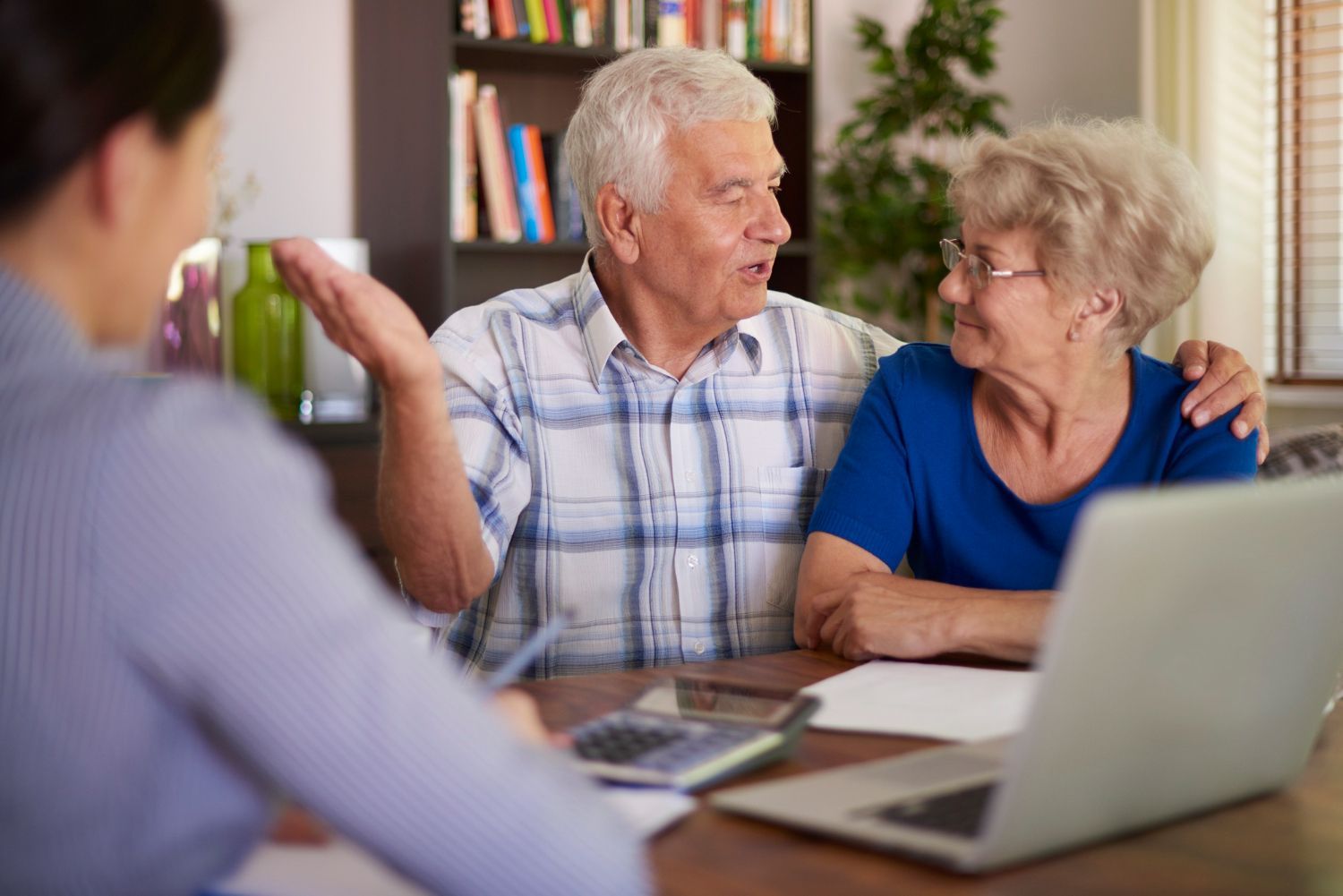 Two people talking at a table with a laptop in a home office setting
