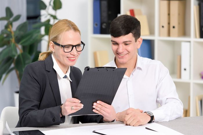 Two coworkers reviewing a clipboard at a desk in an office, smiling and discussing notes