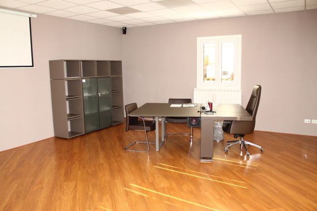 Ufficio vuoto con pavimento in legno, pareti grigie, tavolo, sedie e scaffali vicino a una finestra.
