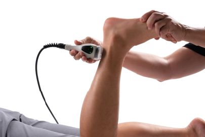Person receiving an ultrasound on their ankle while lying down. A hand holds the device.