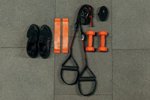 Black shoes, orange resistance bands and dumbbells, and black suspension trainer on gray floor.