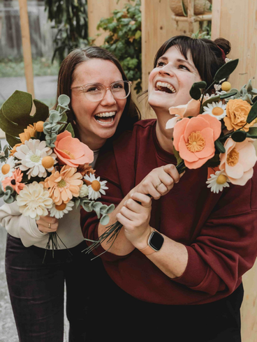 Patricia en Nathalie met allebei een bos viltbloemen in handen lachend