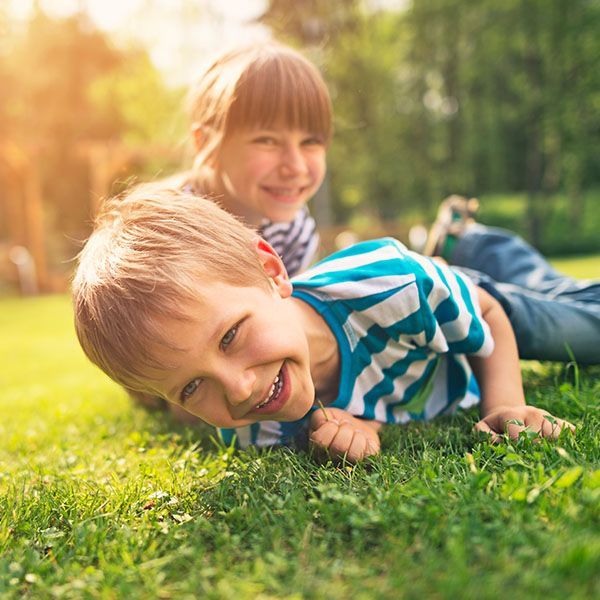 Two children lying on grass, smiling in warm sunlight