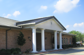 Brick building entrance with white columns and a covered walkway under a blue sky