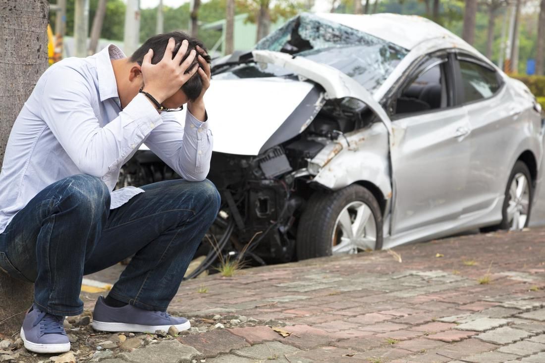 A man is kneeling down in front of a damaged car.