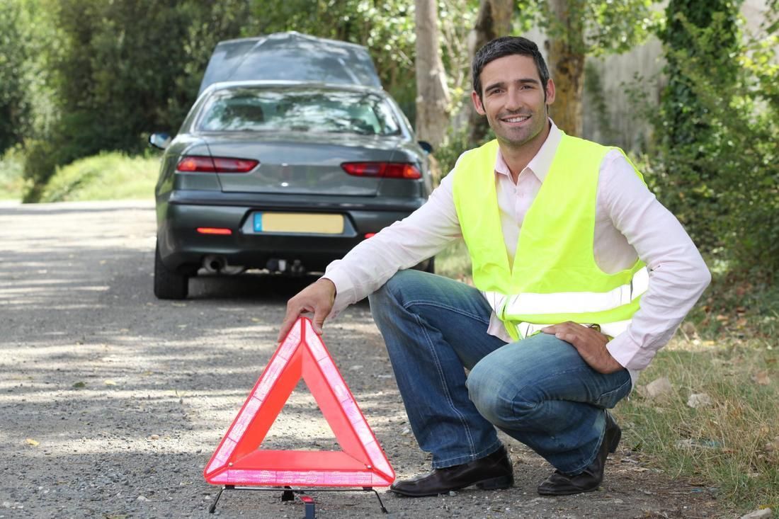 A man in a yellow vest is kneeling next to a warning triangle.