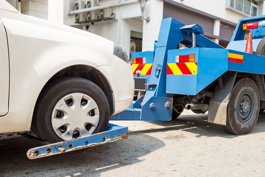 A white car is being towed by a blue tow truck.