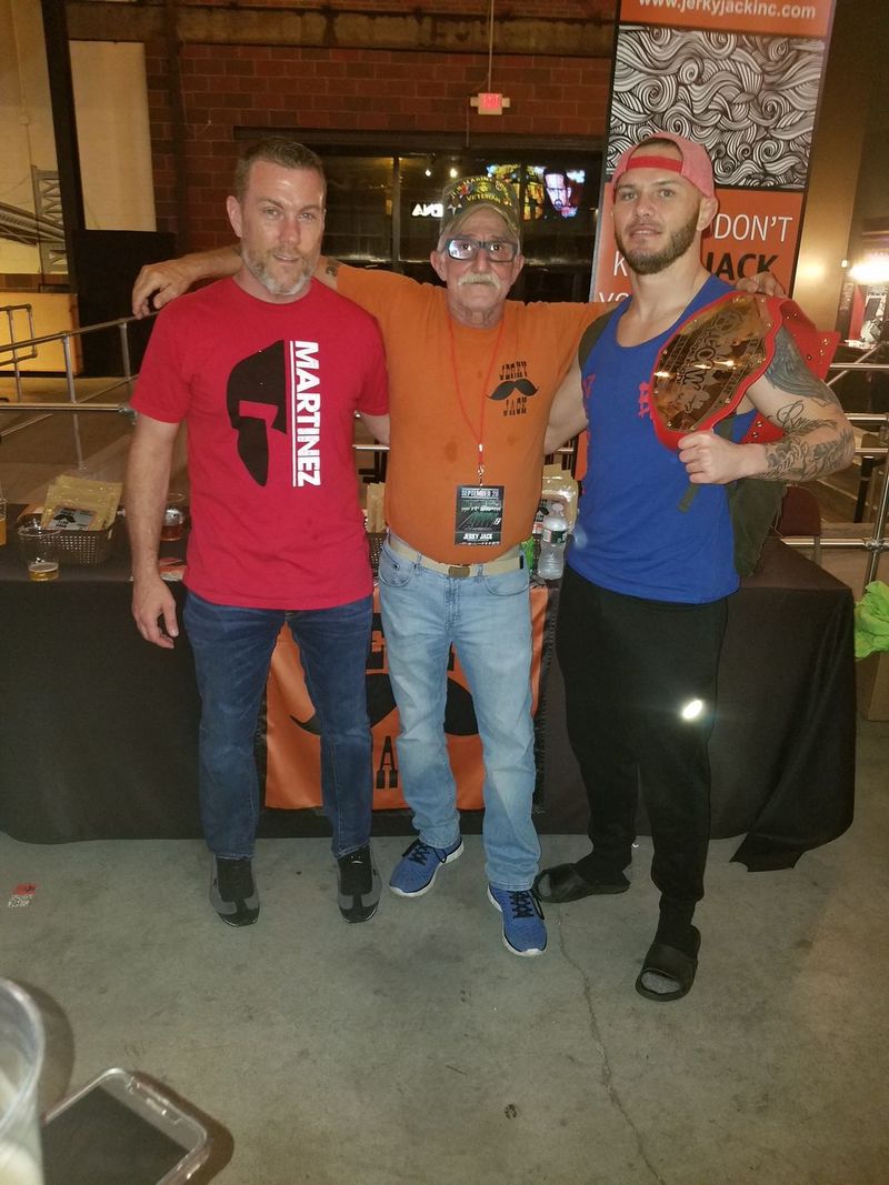 A man in a martinez shirt poses with two other men