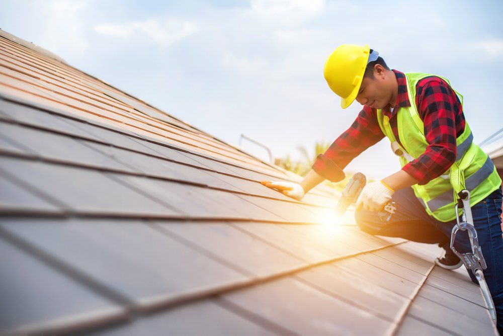 Worker in yellow hard hat installing solar panels on a rooftop at sunset