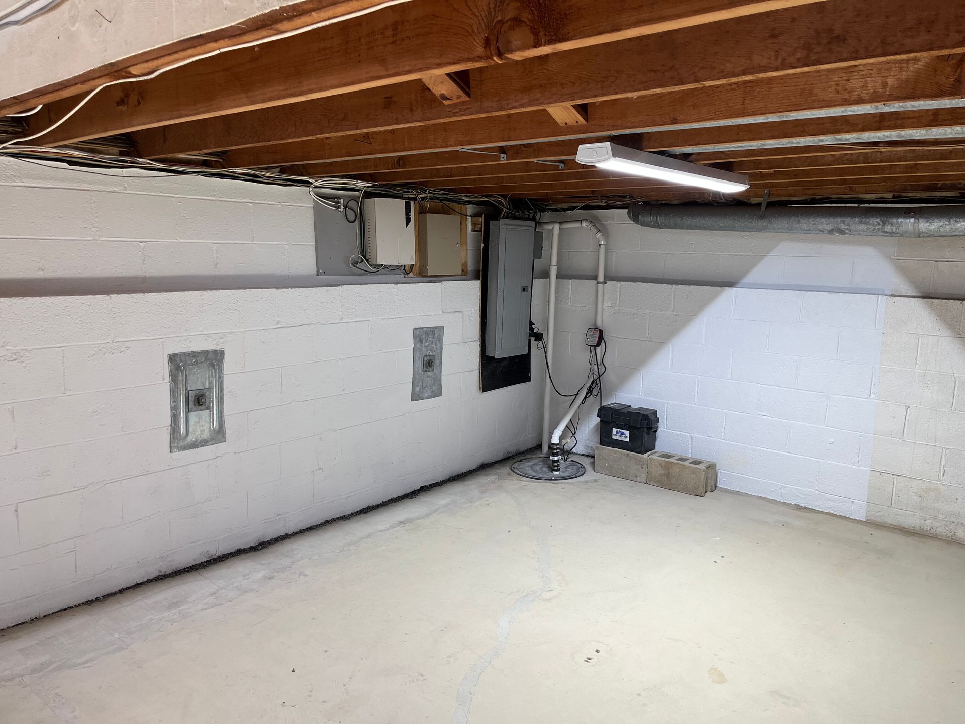 Empty basement corner with exposed beams, white walls, and a fluorescent light fixture.