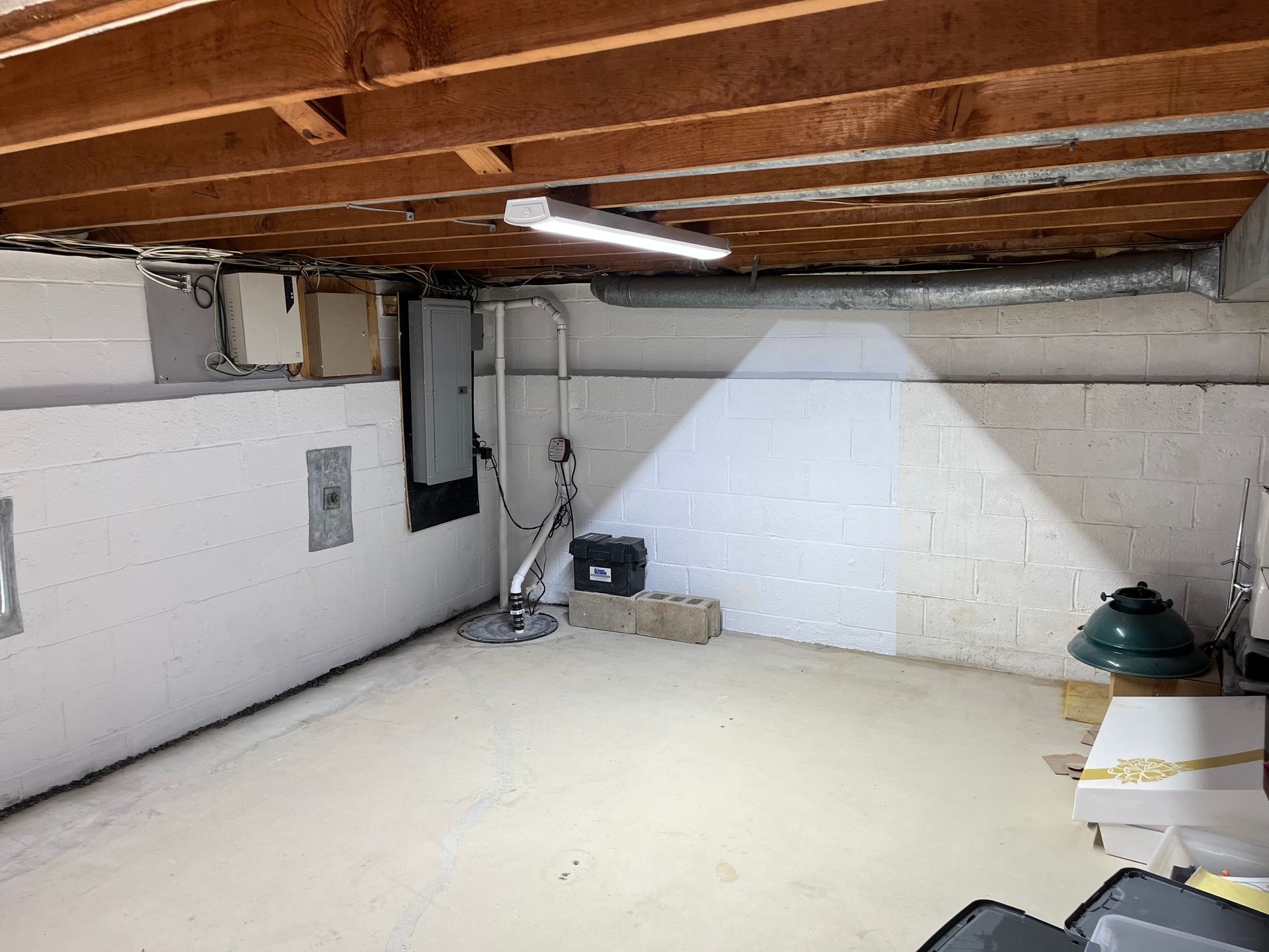 Empty basement with white cinderblock walls, exposed wooden ceiling joists, and a bright floor light near the wall