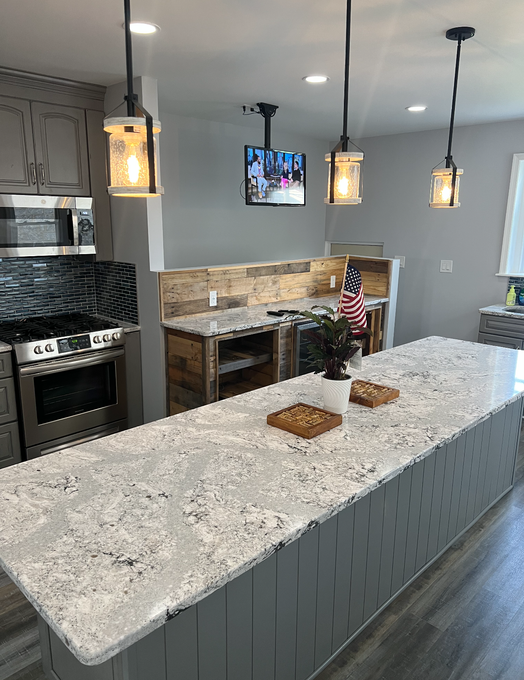 Modern kitchen with granite island, pendant lights, wall-mounted TV, and a cozy breakfast nook