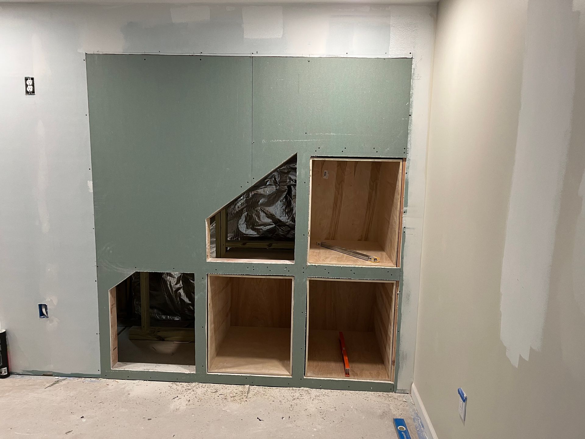 Partially finished wall with four box openings in a gray room during renovation