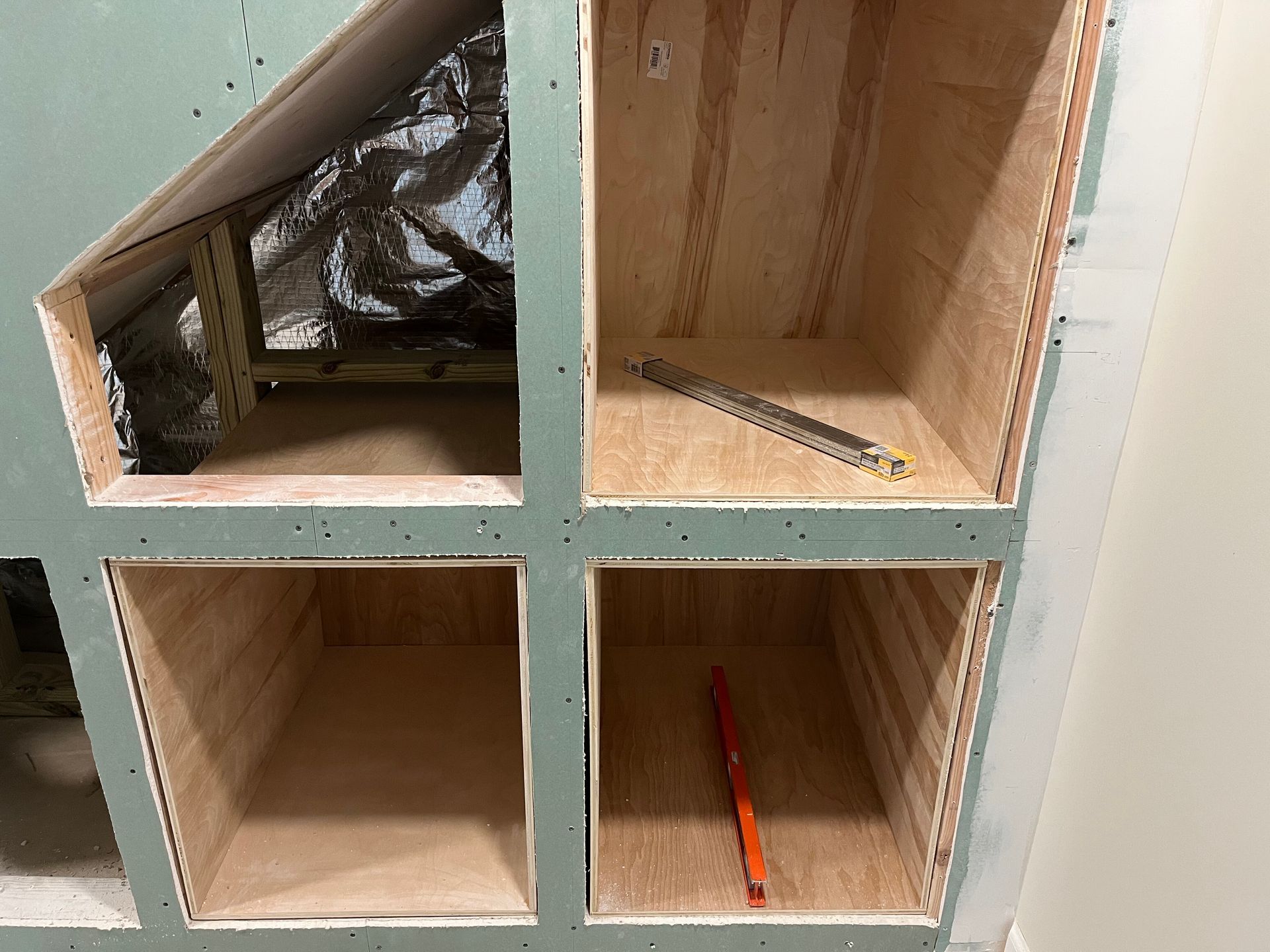 Four-cubby wooden shelf with a foil-lined top-left compartment and pens in two lower compartments.