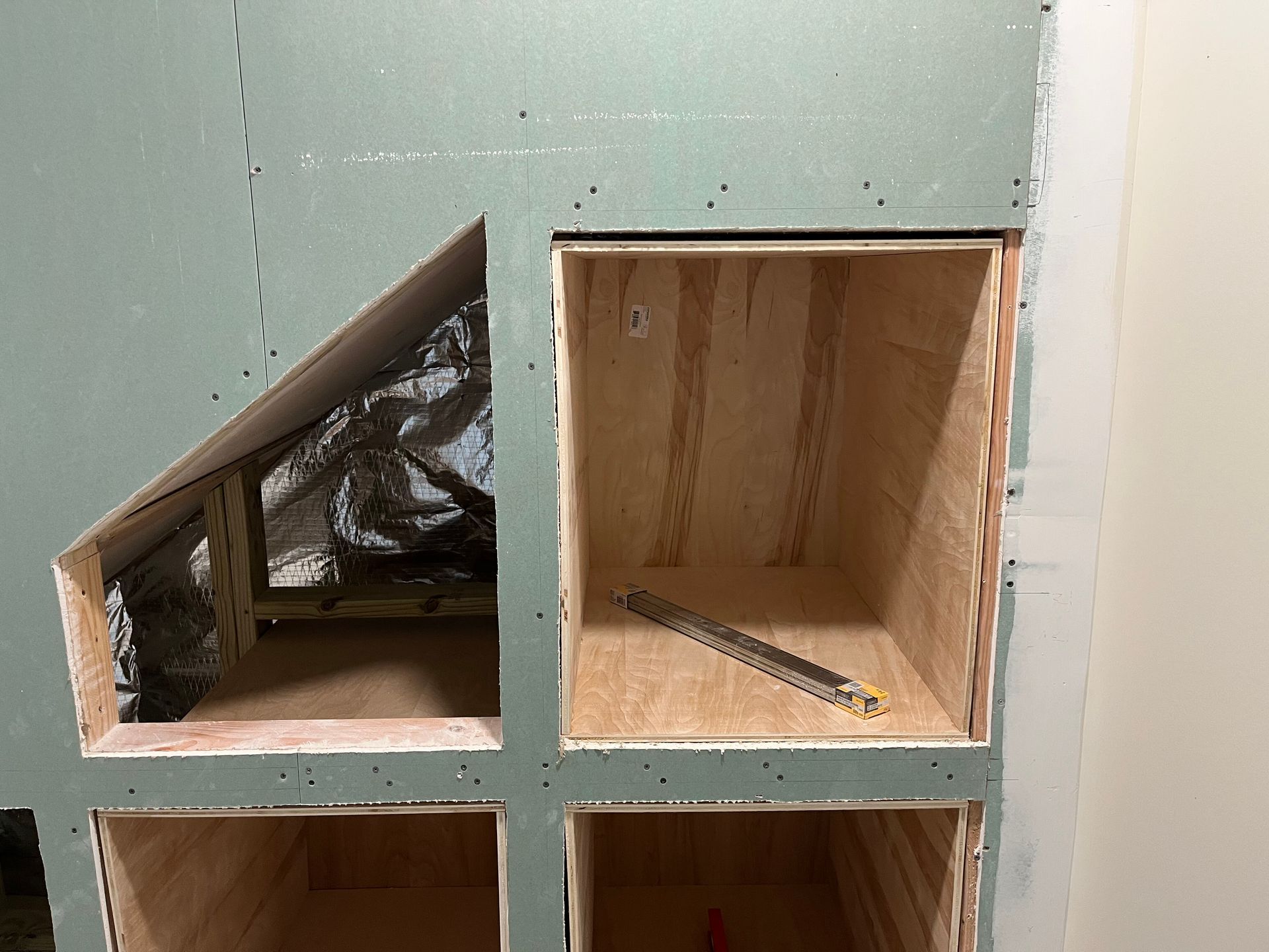 Two small wooden cabinet compartments, one slanted and lined with black plastic, against a green wall.