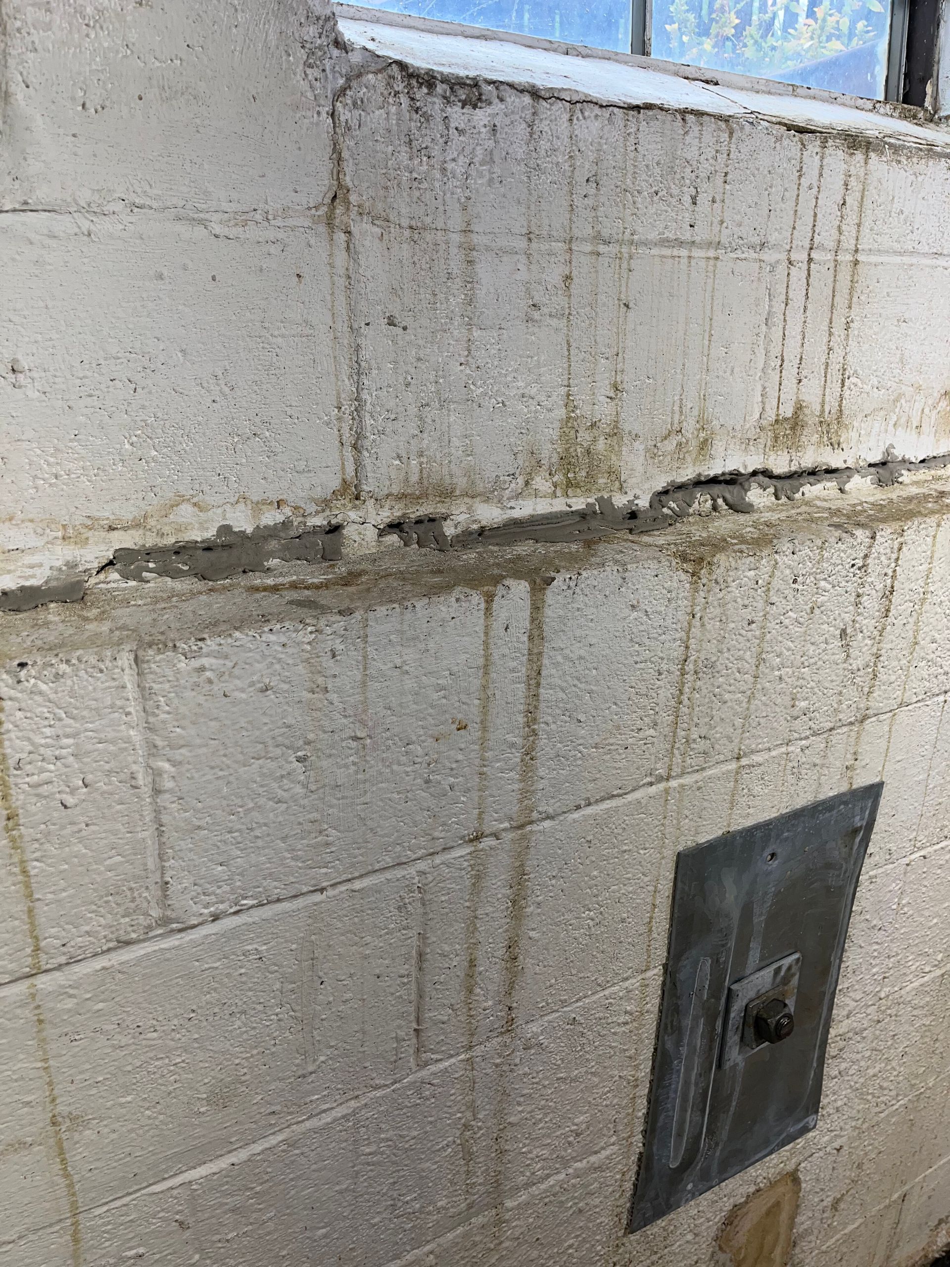 Close-up of a stained concrete wall with a horizontal crack and a small metal fixture near the bottom.