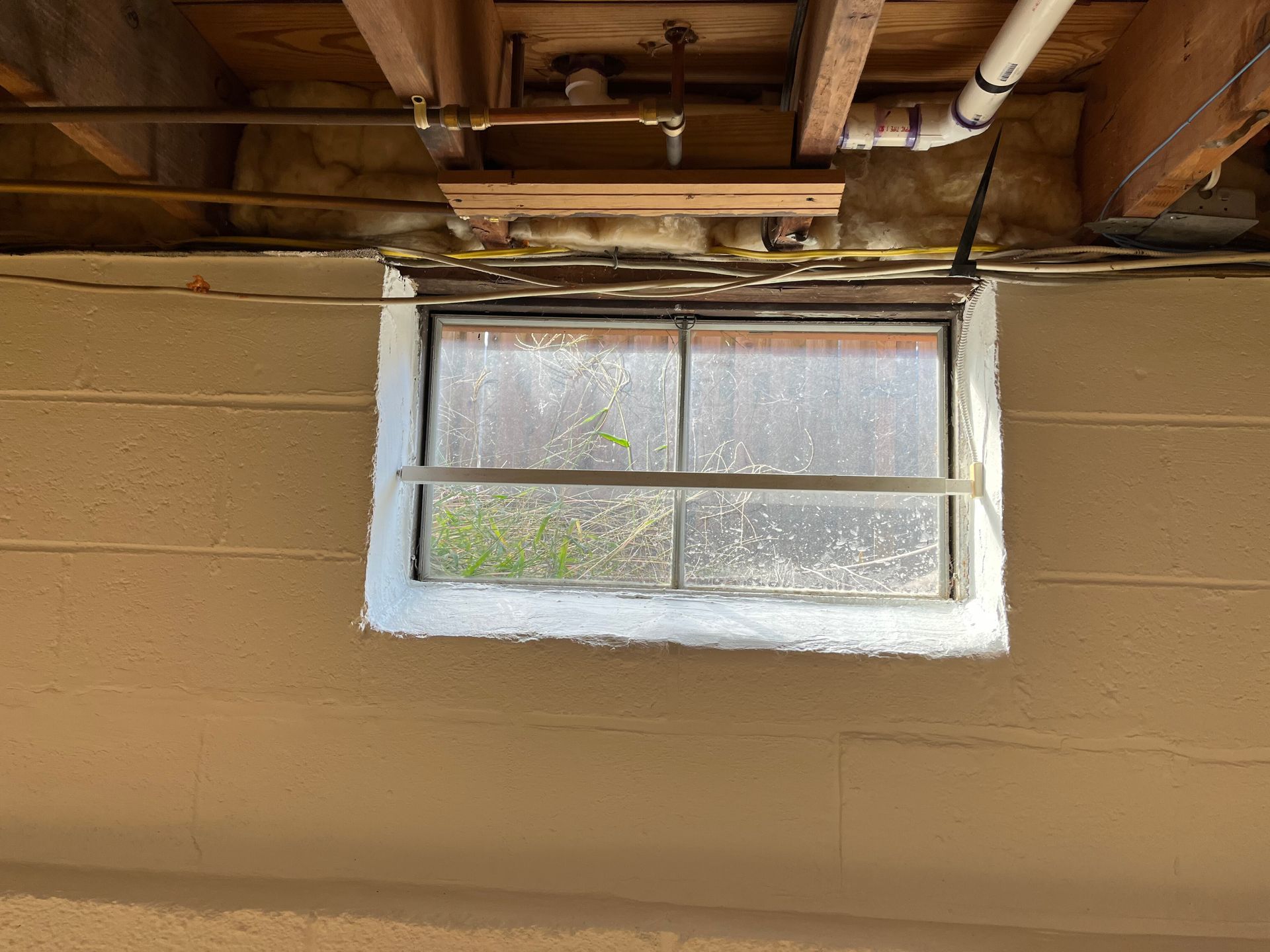 Basement window under exposed ceiling joists, with painted cinder block wall and white trim