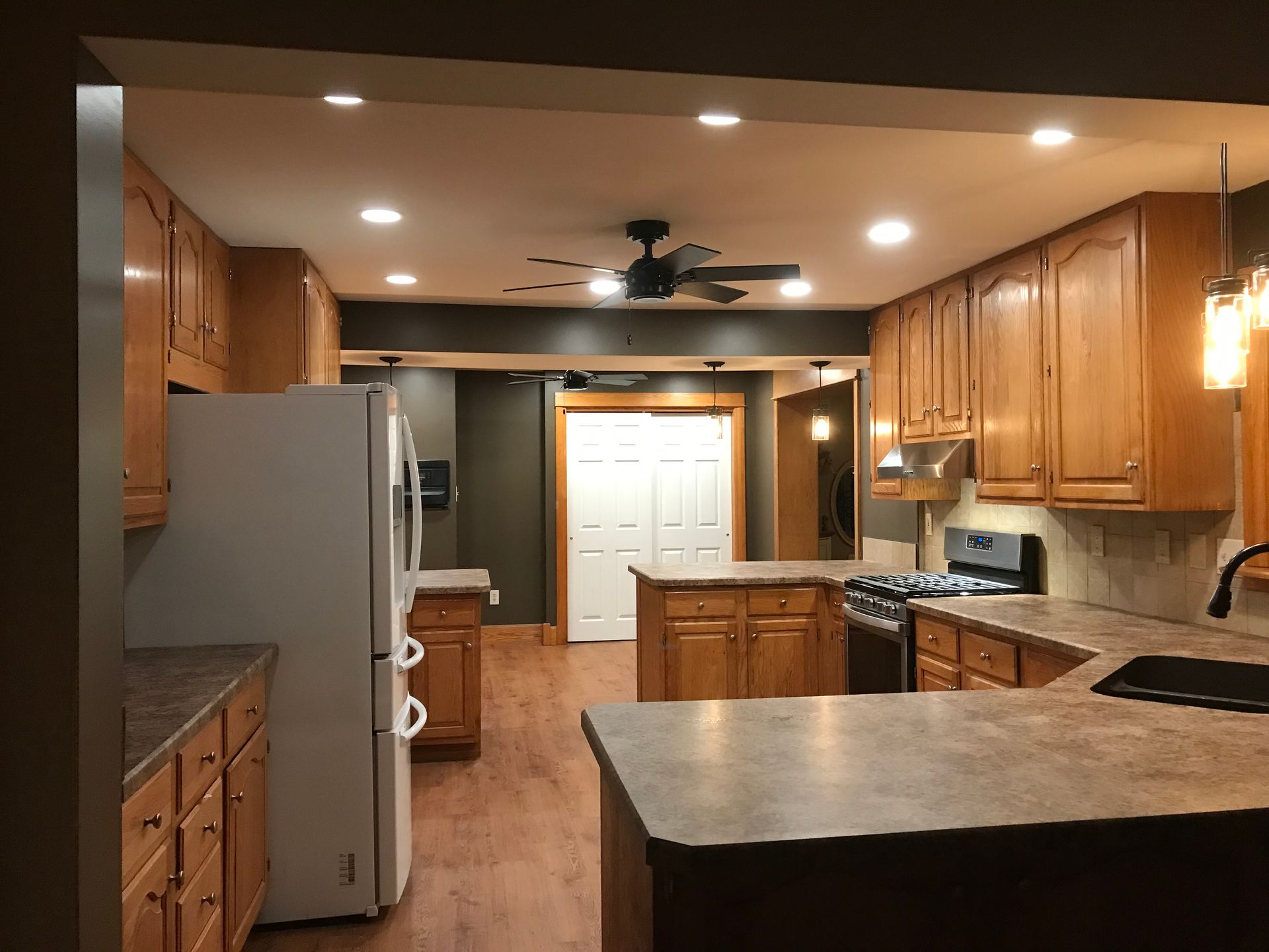 Warm kitchen with wood cabinets, island, white door, ceiling fan, and stainless steel refrigerator