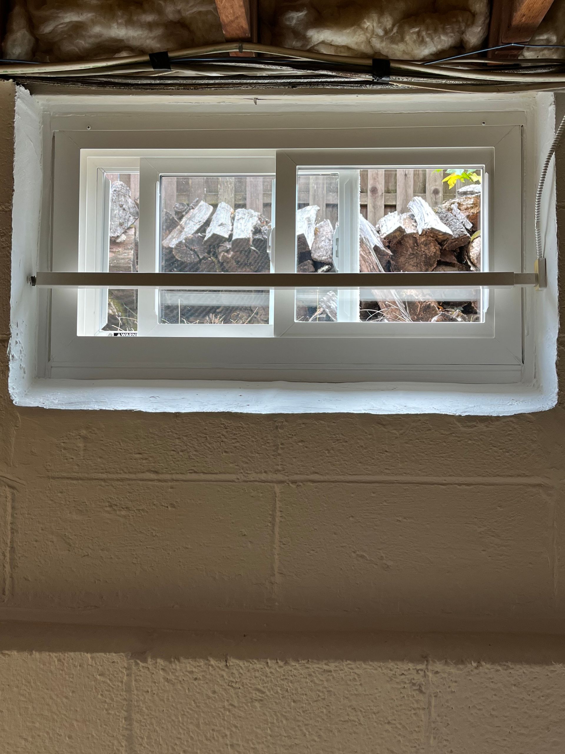 Small white basement window set in tan wall, with snow visible outside