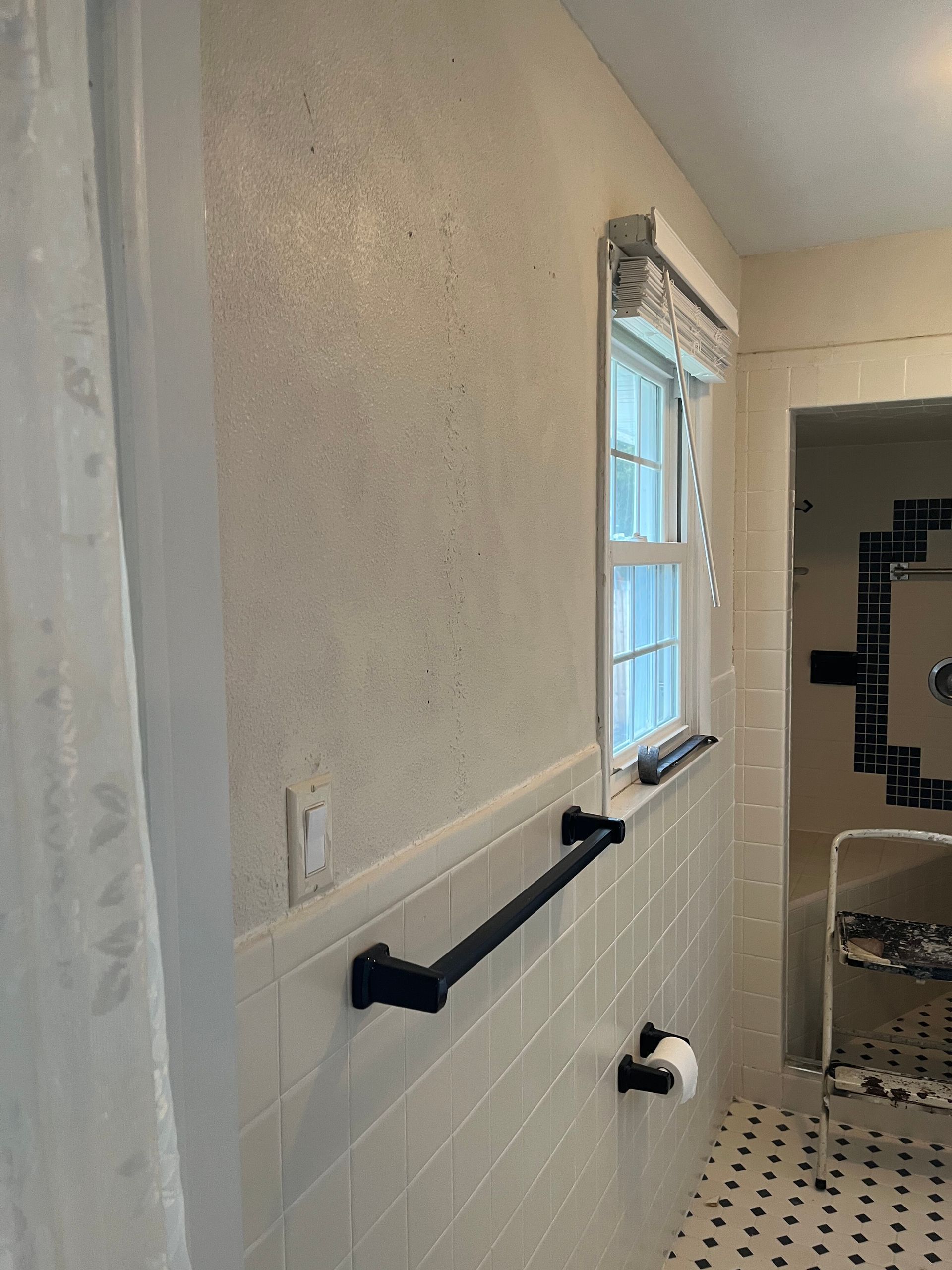 Bathroom with grab bars, tiled wall, window, and patterned floor.