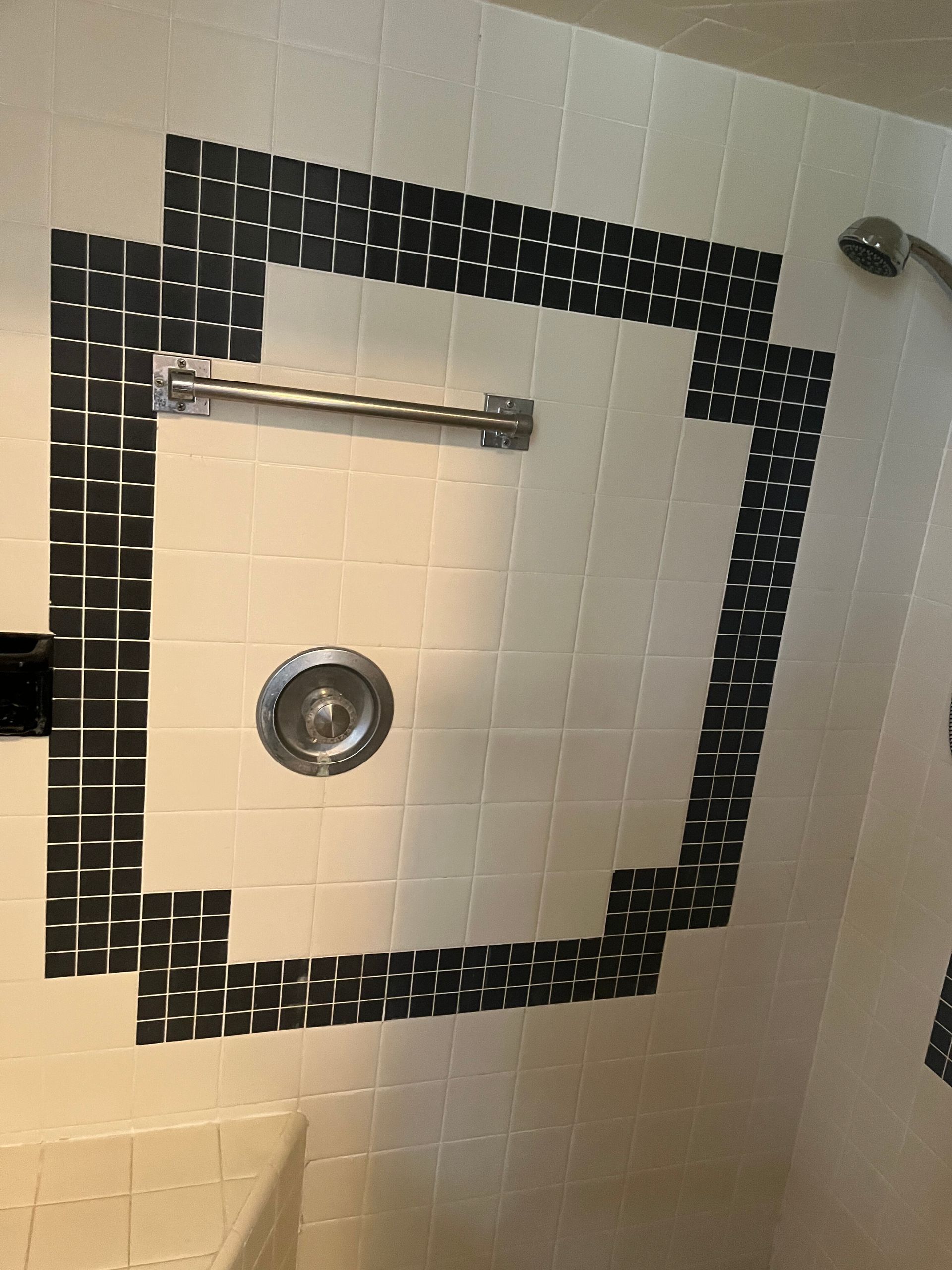 Bathroom shower stall with white tiles and a black border, showing a tub spout and circular drain cover.