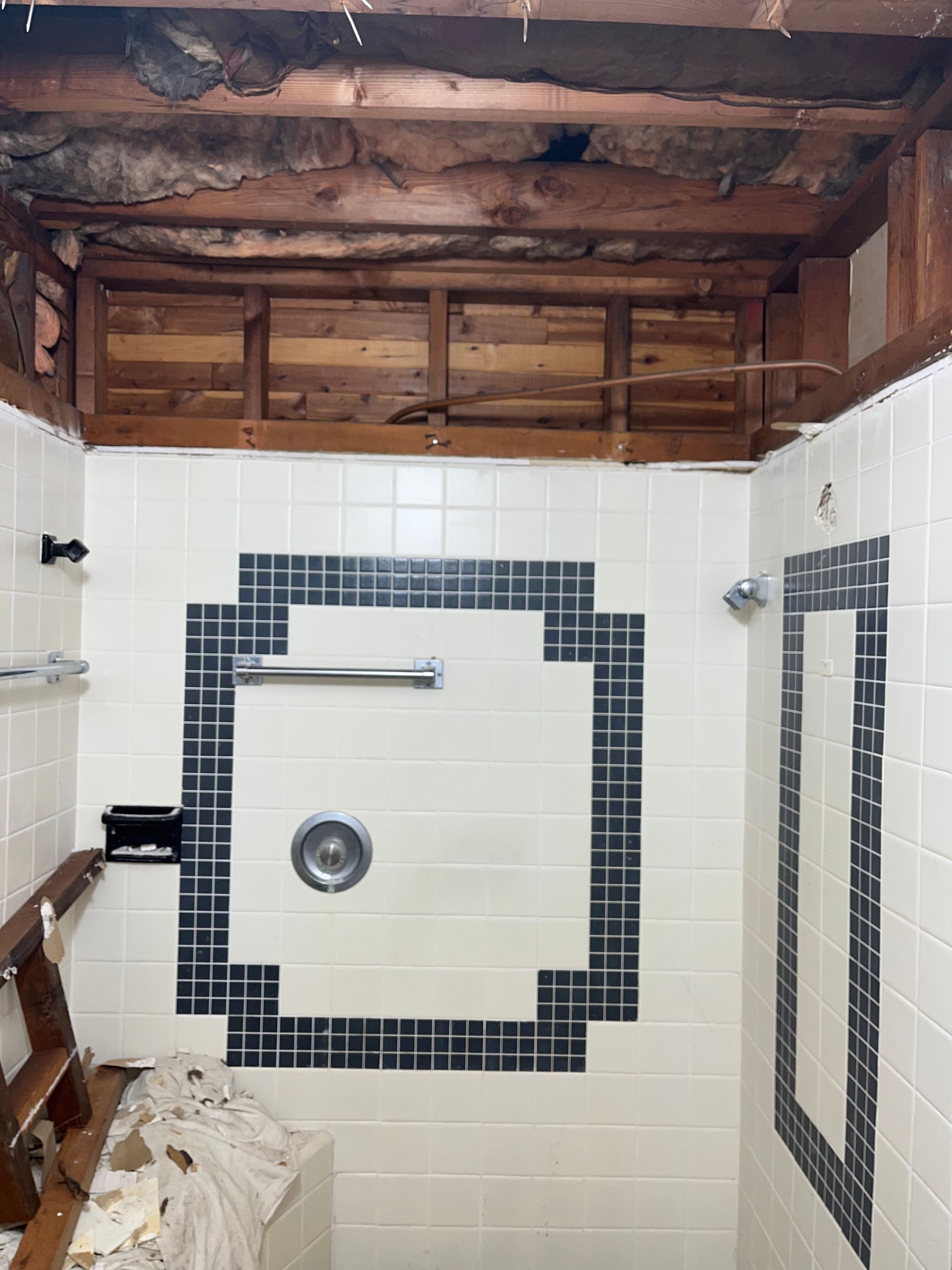 Partially demolished shower with exposed wood ceiling and white tile walls with black trim