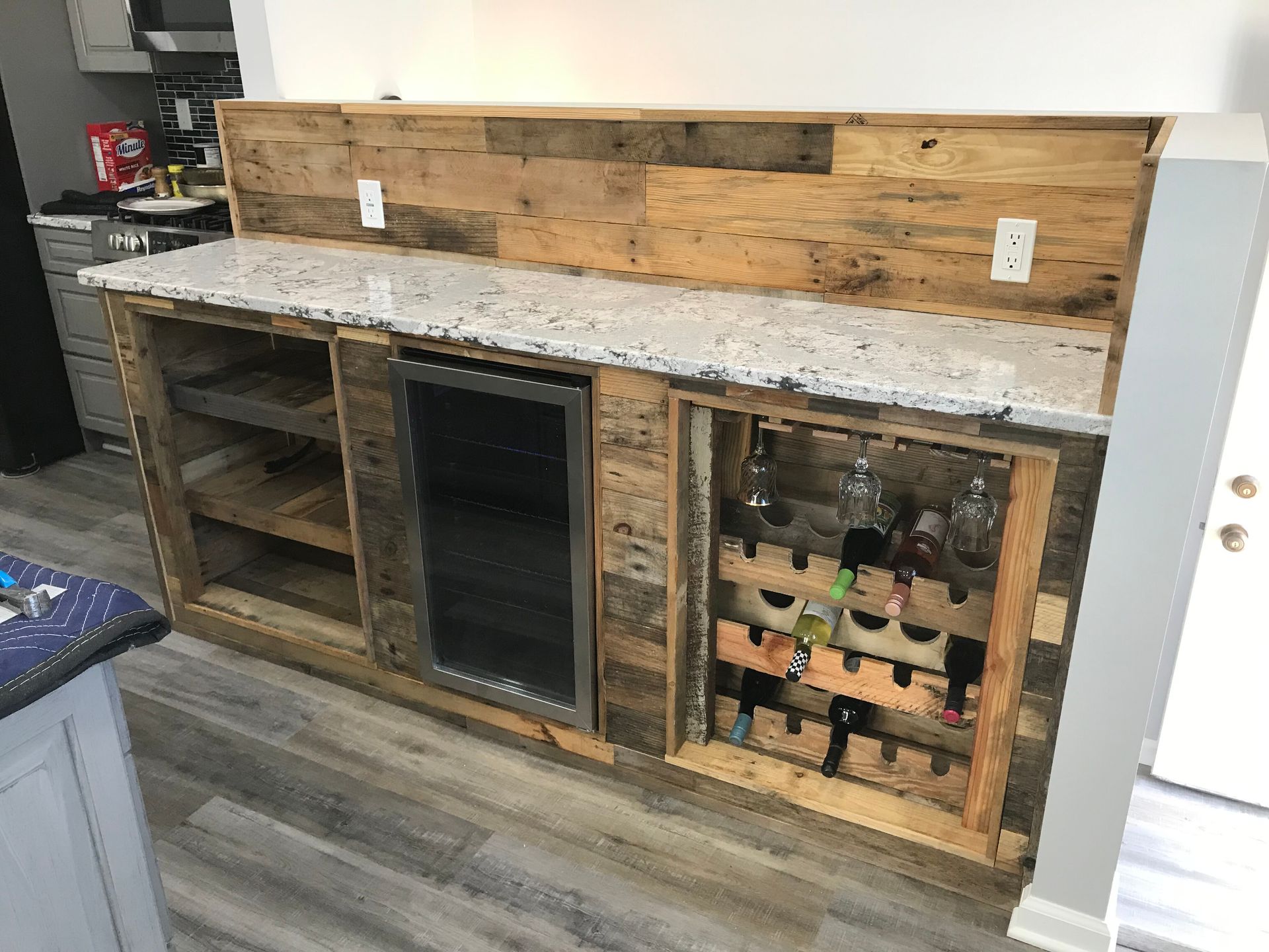 Rustic kitchen counter with wood cabinets, granite top, open shelves, and wine rack against a wood backsplash
