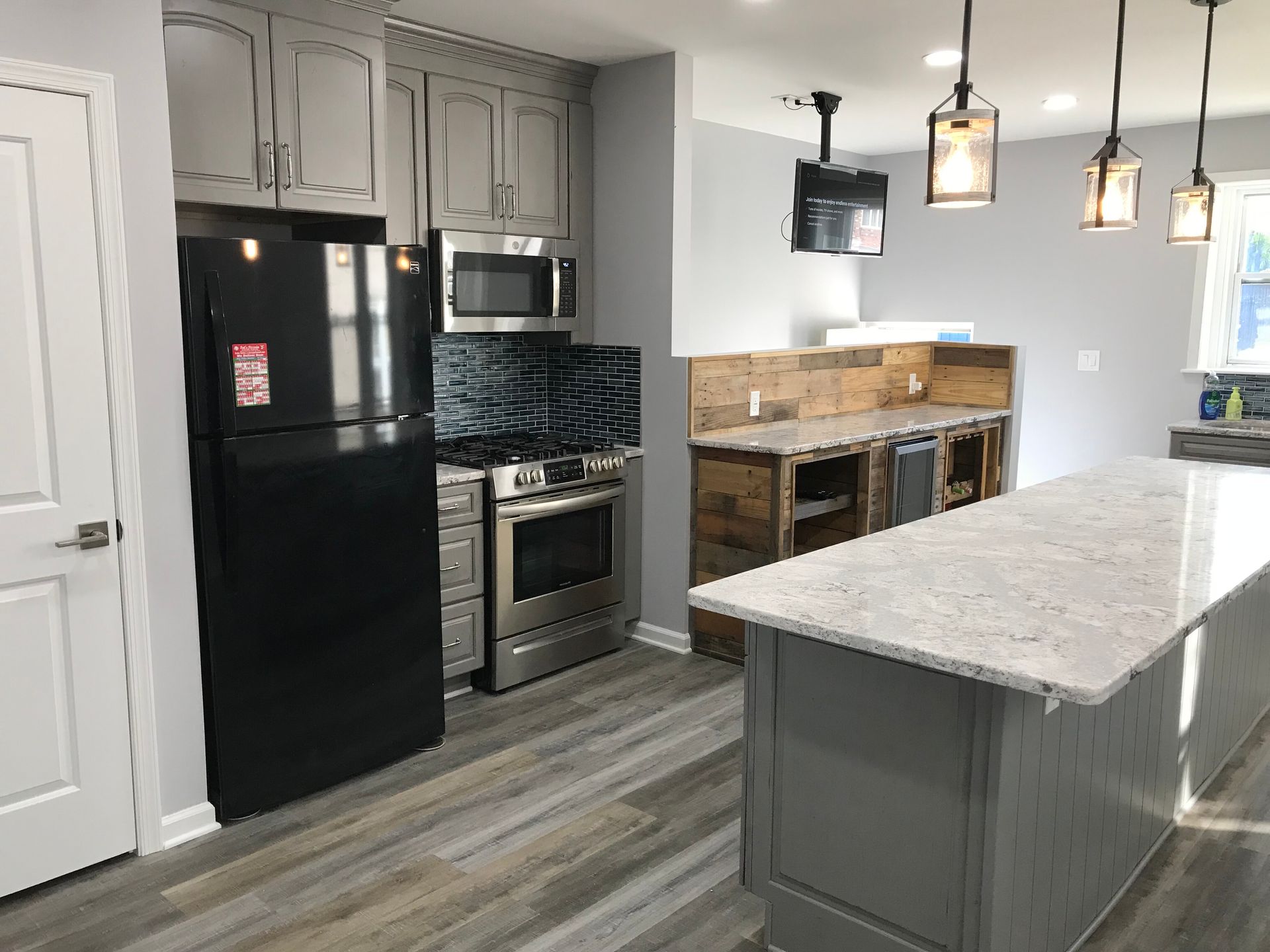 Modern kitchen with black appliances, gray cabinets, marble island, and pendant lights