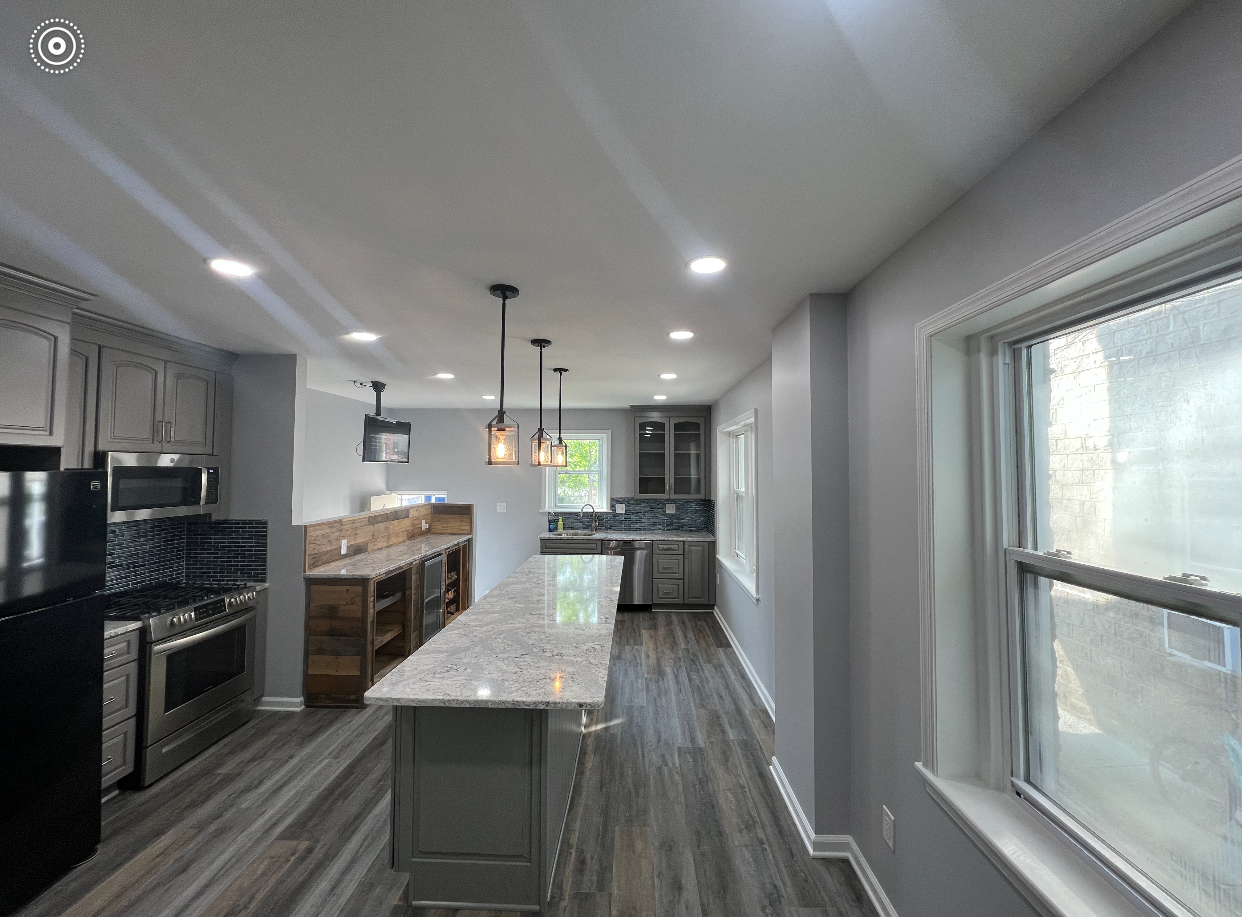 Modern kitchen with gray cabinets, marble island, stainless appliances, and recessed lighting.