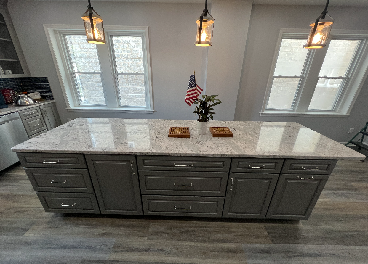 Kitchen island with white marble countertop, dark gray cabinets, and pendant lights in a bright kitchen