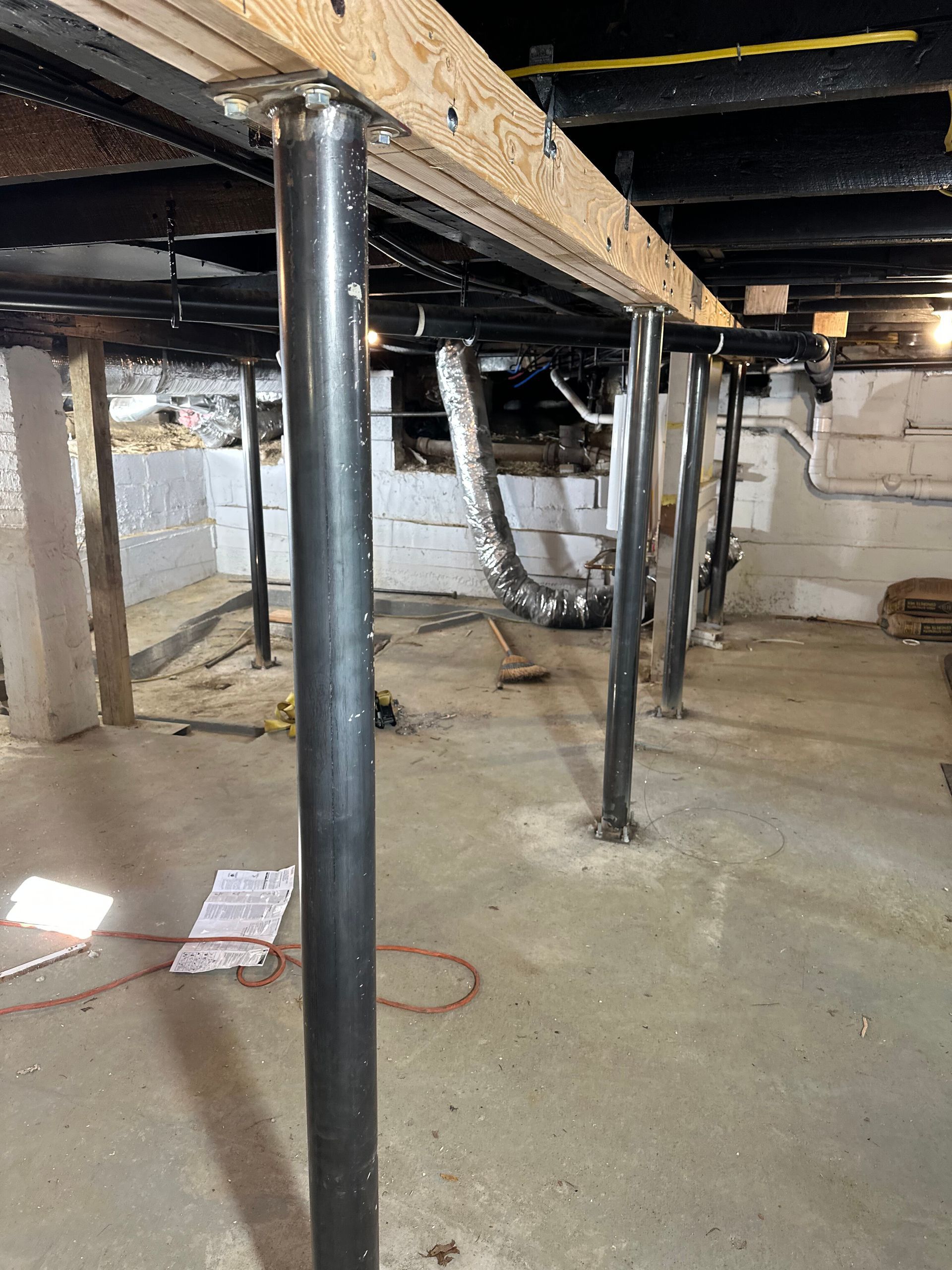Basement crawlspace with black support posts, exposed beams, and concrete floor.