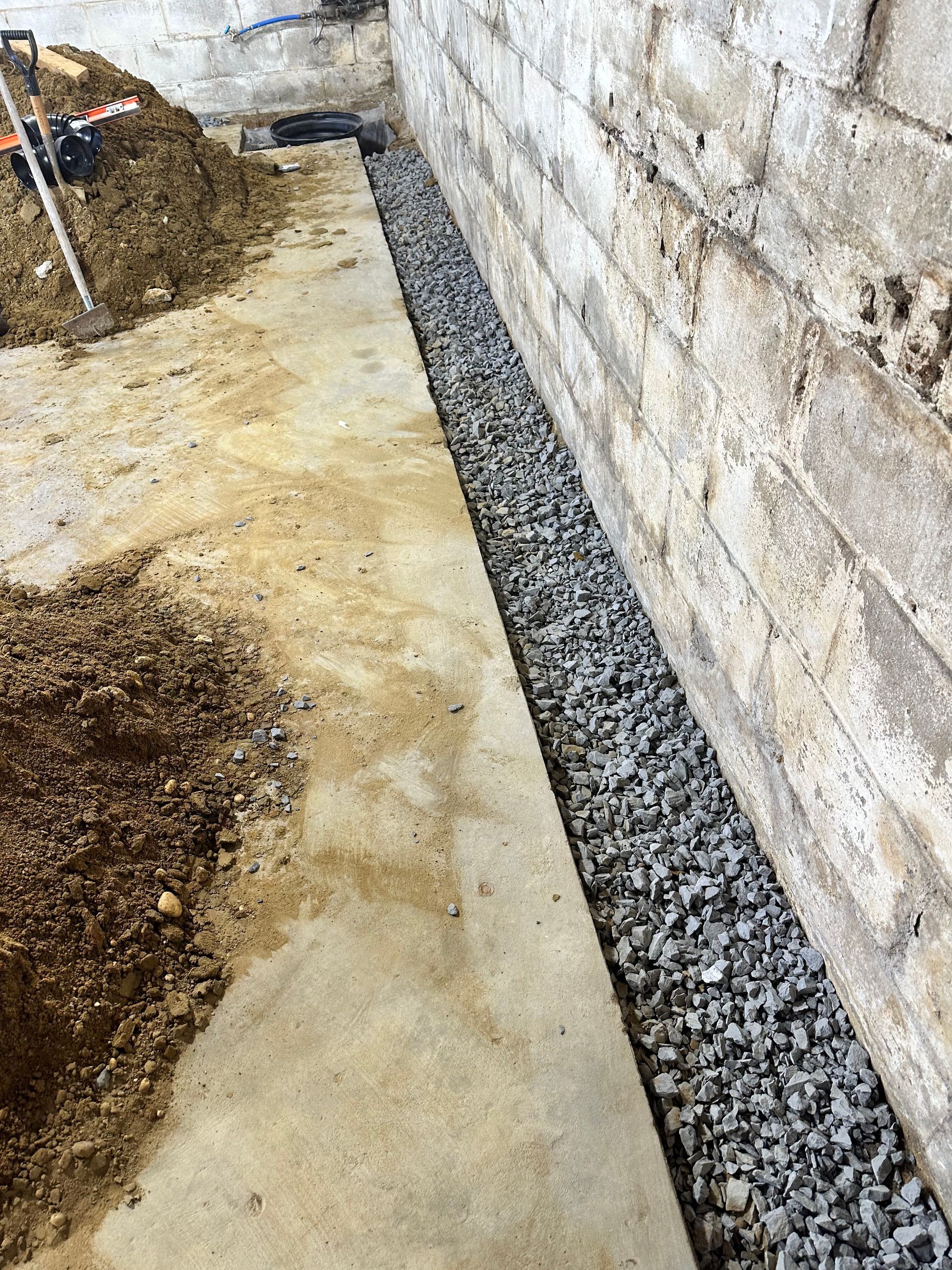 Concrete walkway beside cinder block wall with gravel drainage trench and dirt piles during construction