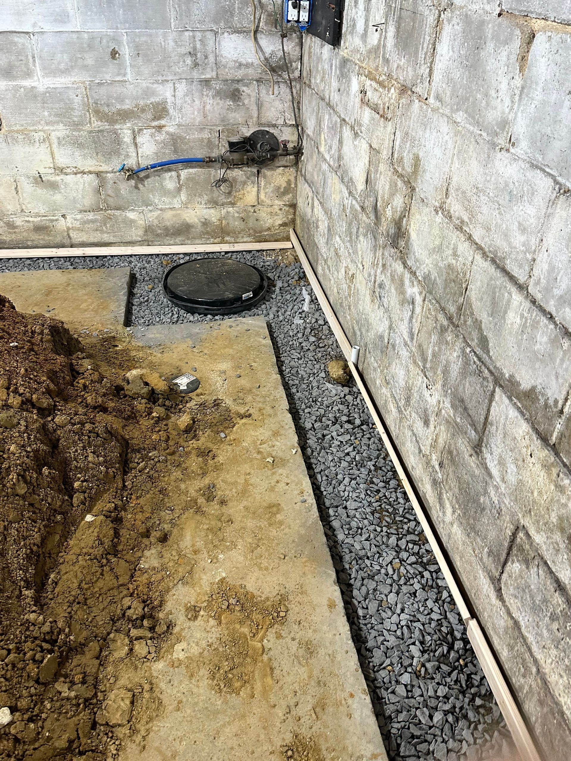 Basement corner with concrete walls, gravel trench, and circular drain cover
