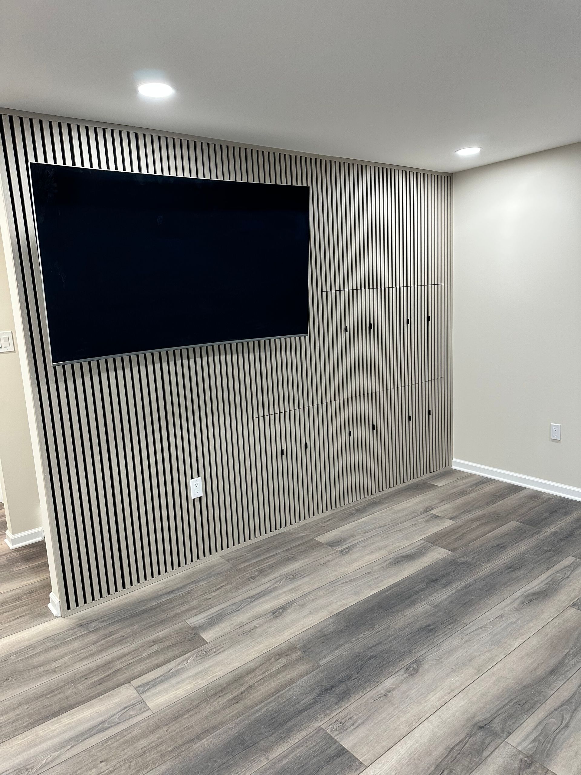 Modern living room with striped accent wall, large wall-mounted TV, gray carpet, and recessed lighting