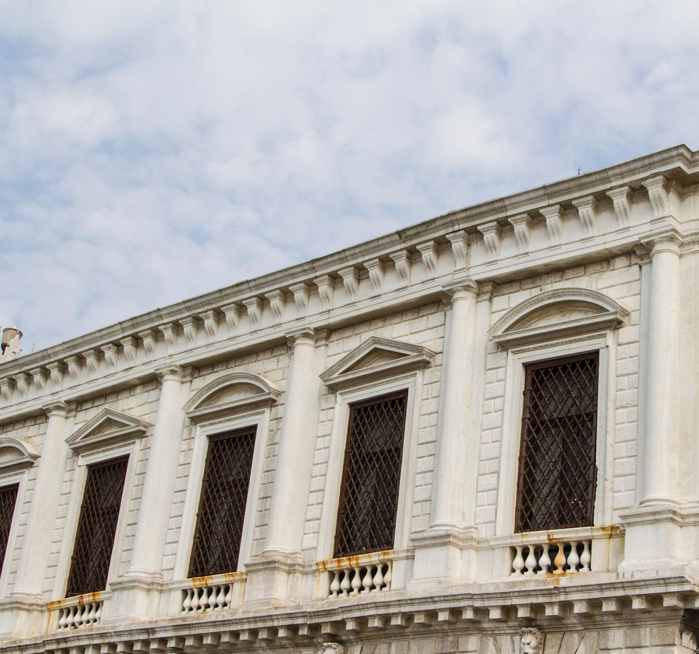 Facciata bianca e riccamente decorata dell'edificio, con alte finestre ad arco e colonne ornamentali sotto un cielo nuvoloso.
