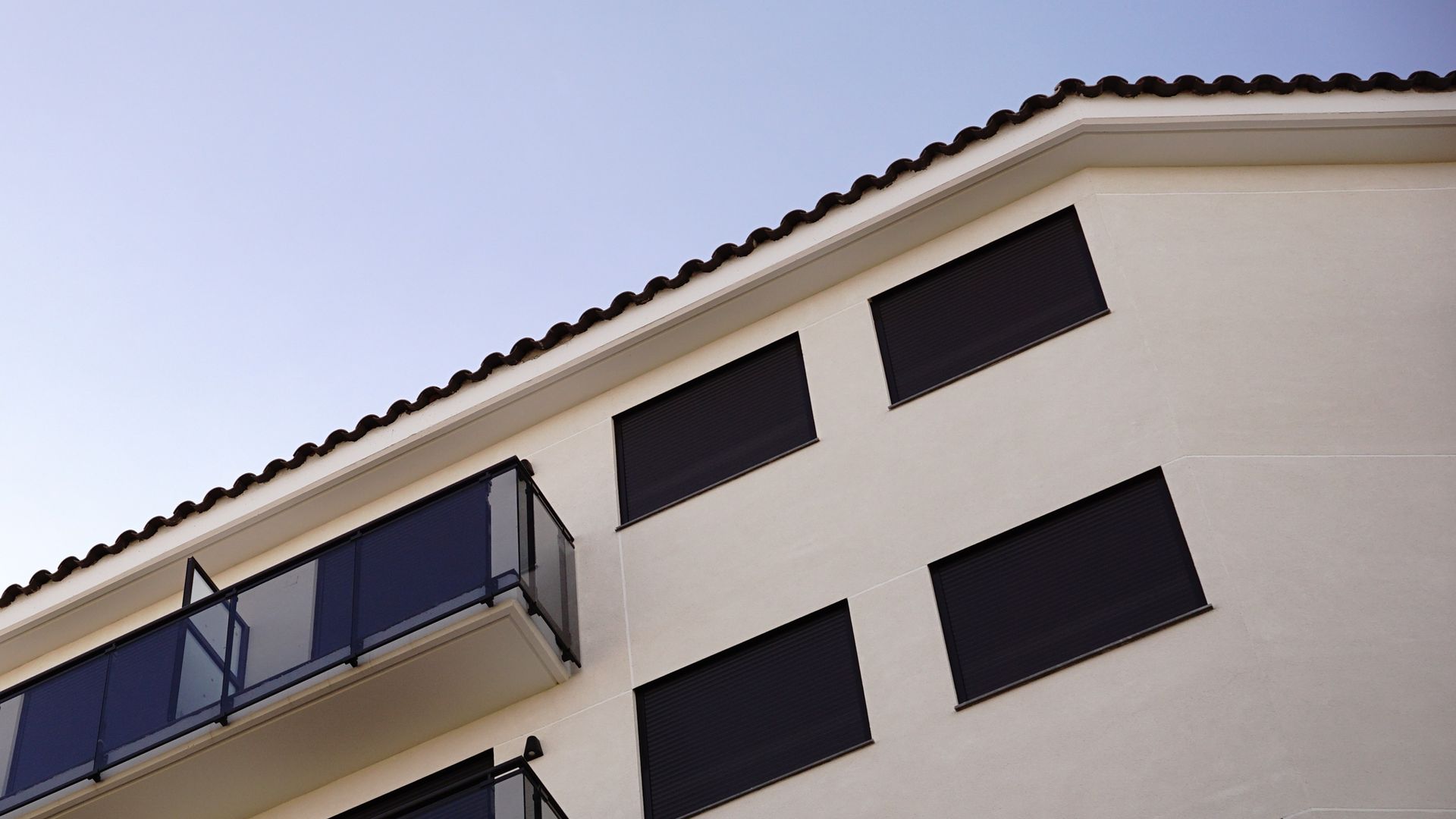 Moderno palazzo residenziale bianco con finestre scure e balcone in vetro, visto dal basso.