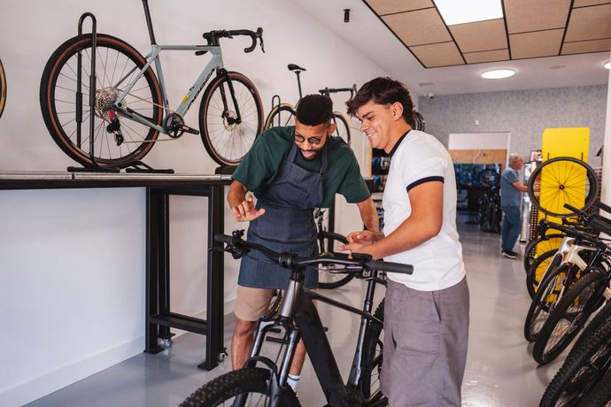 Two people examining a black bicycle in a bike shop, with other bikes displayed nearby.