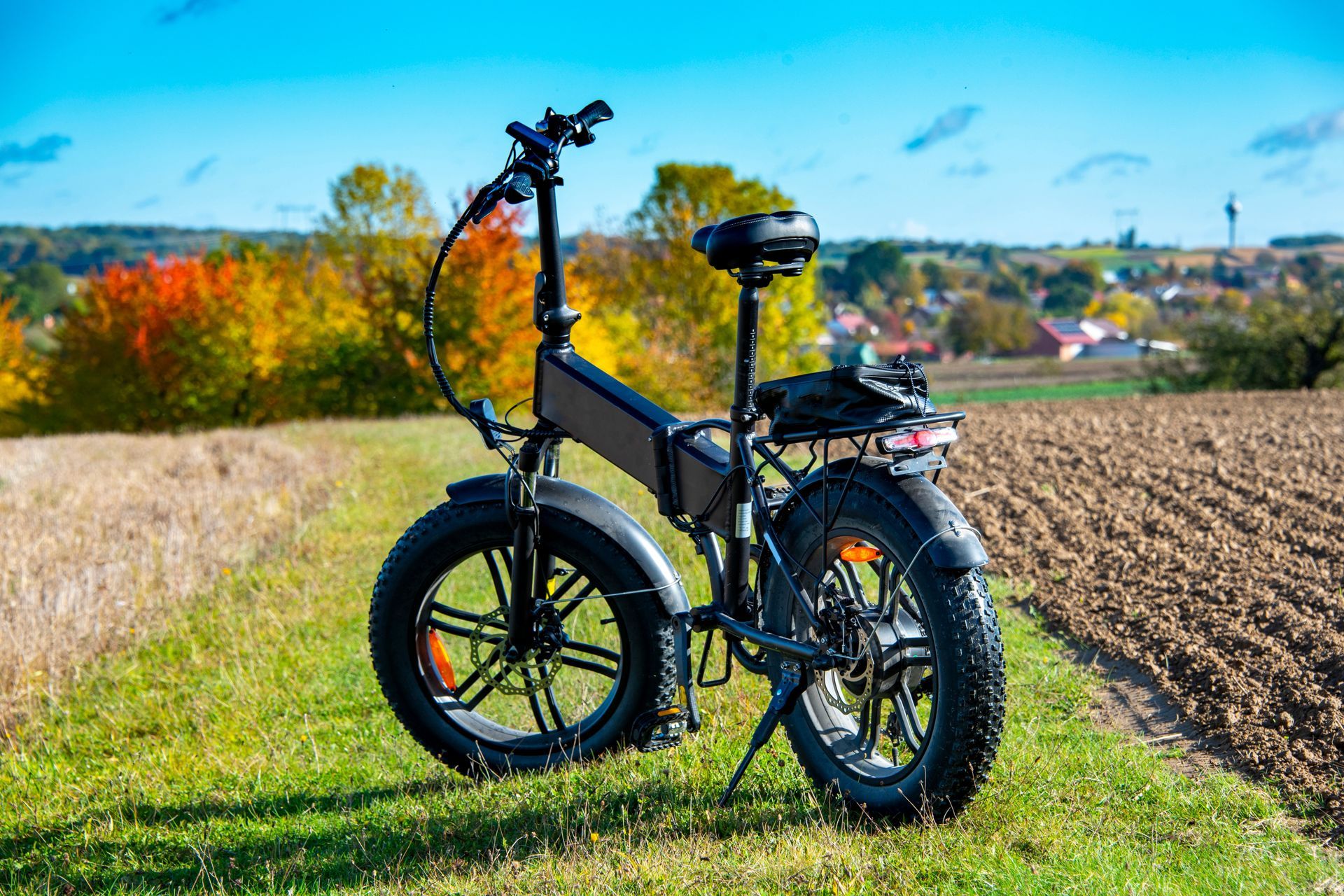 Black folding e-bike on a grassy path beside a field, with a countryside landscape in the background