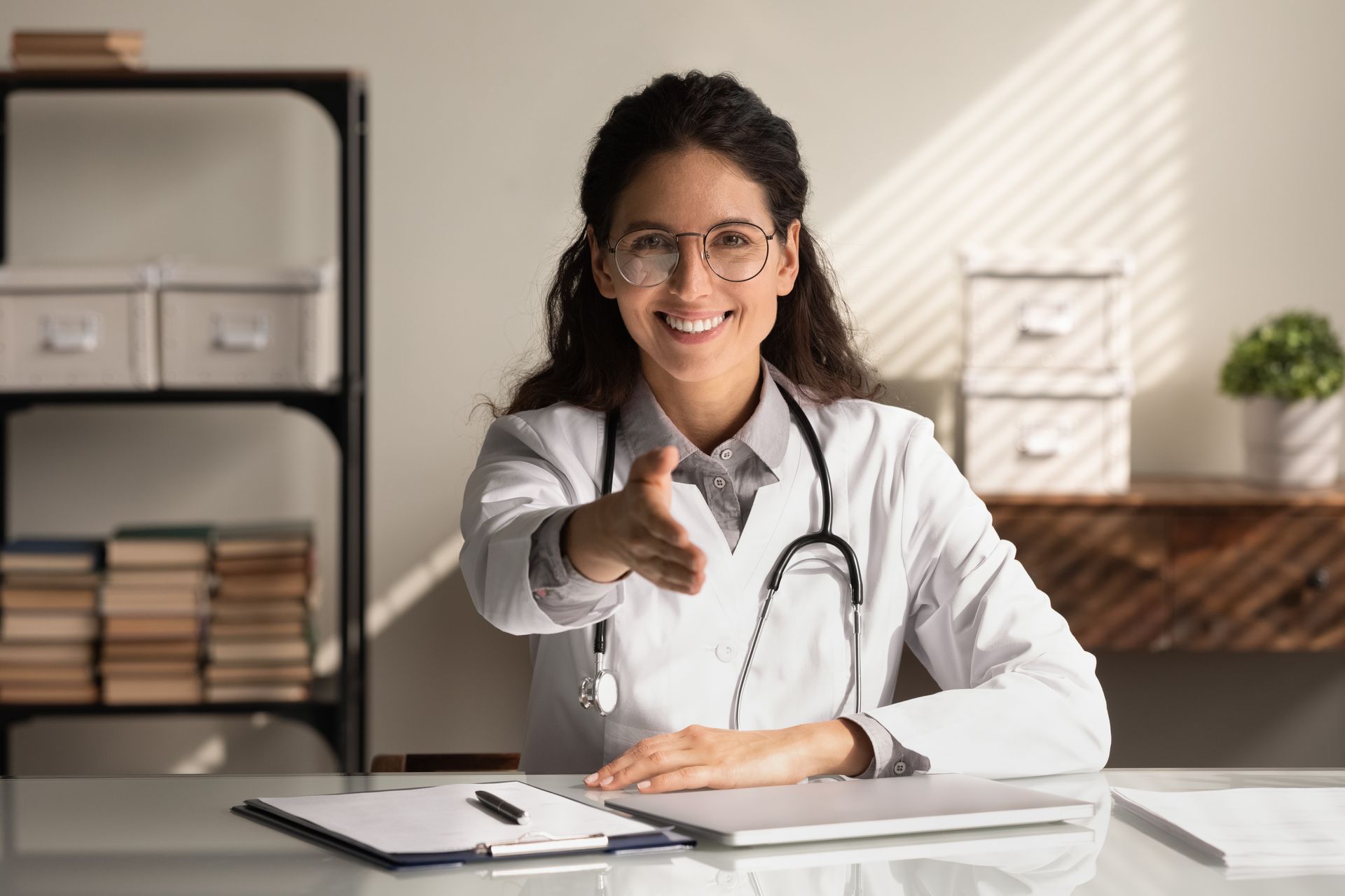 Portrait of young female doctor in white uniform stretch hand for handshake greet get acquainted with patient in clinic