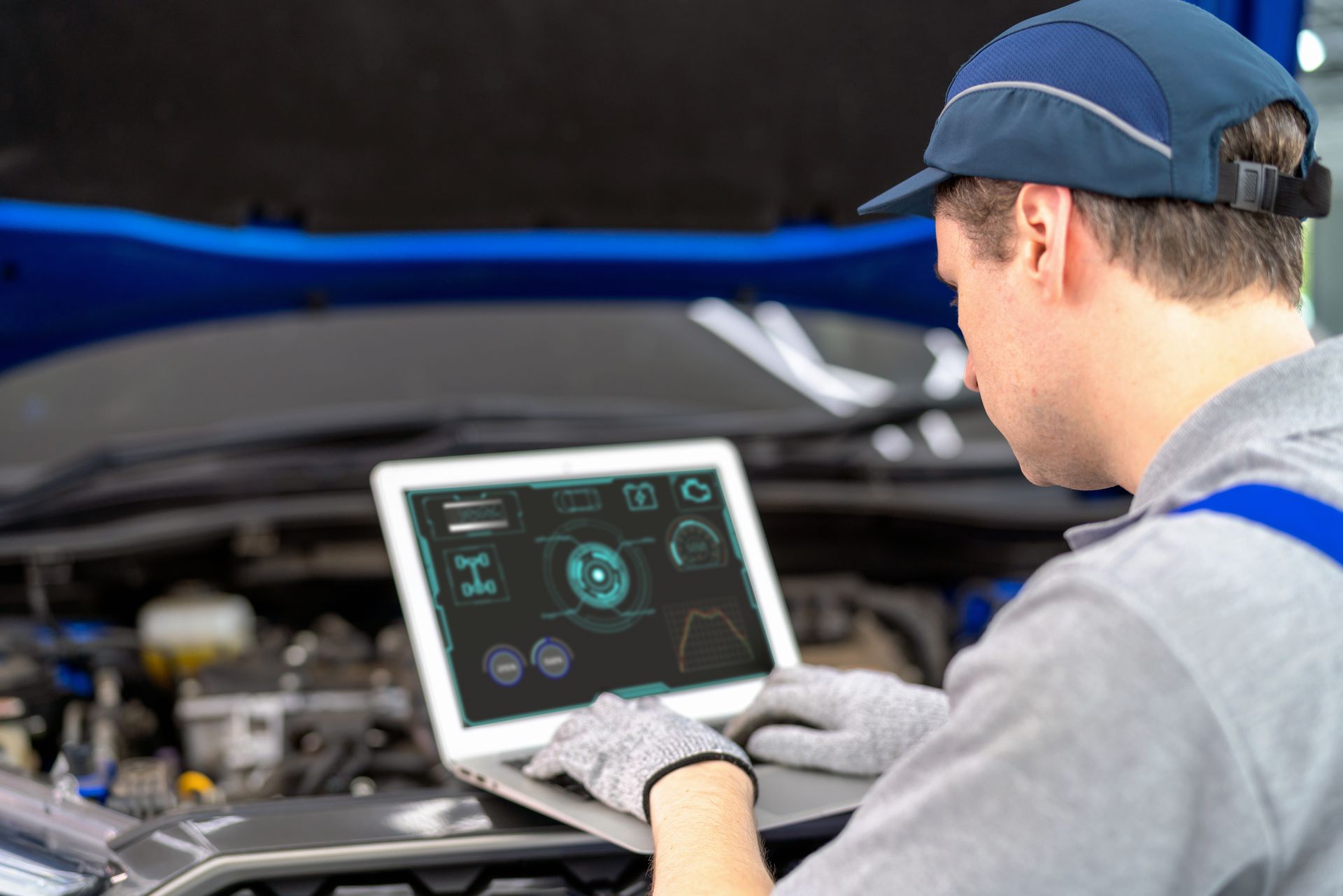 A man is using a laptop computer while working on a car.