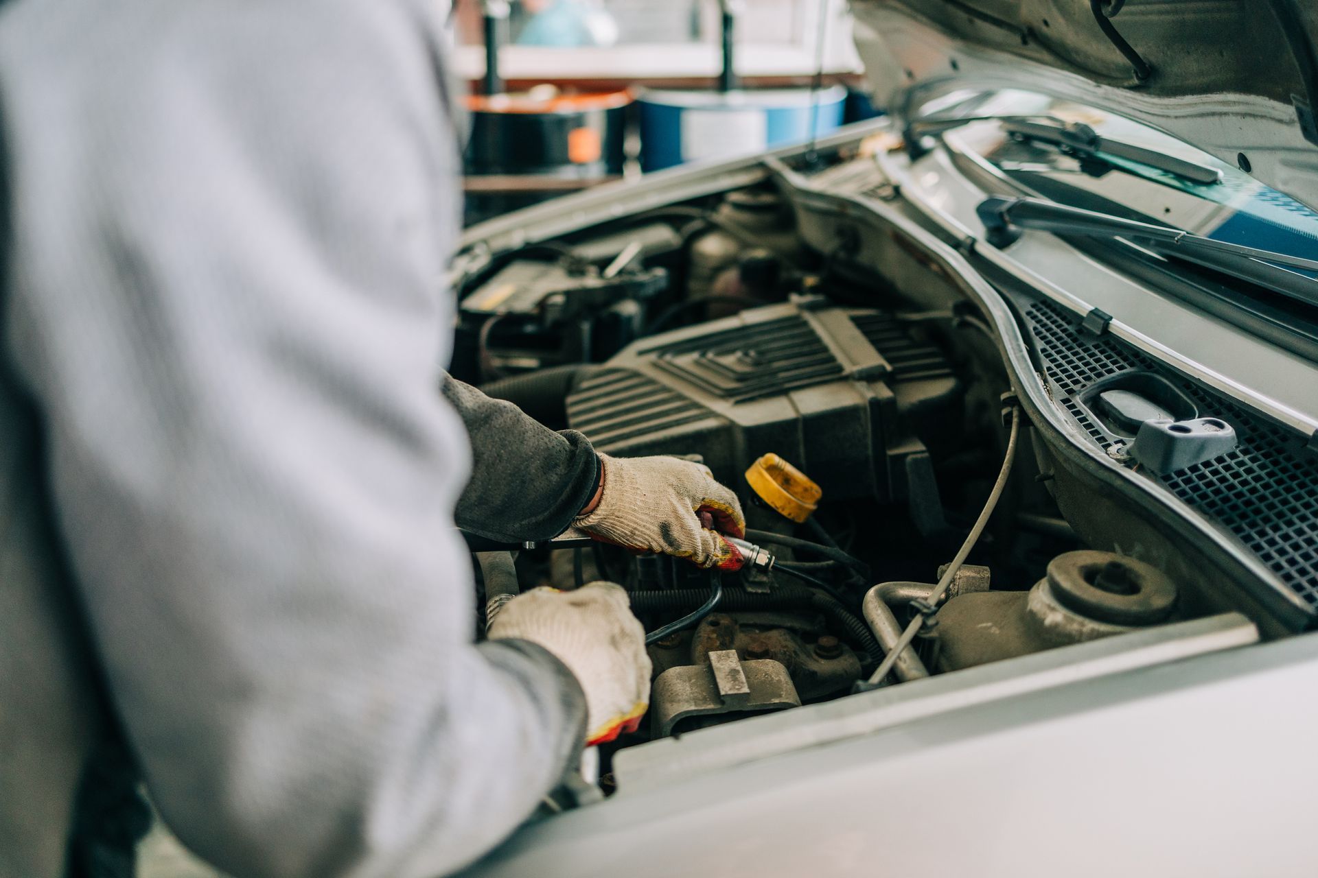 A mechanic uses tools to fix the inside of a silver car’s hood, inside a car repair shop.