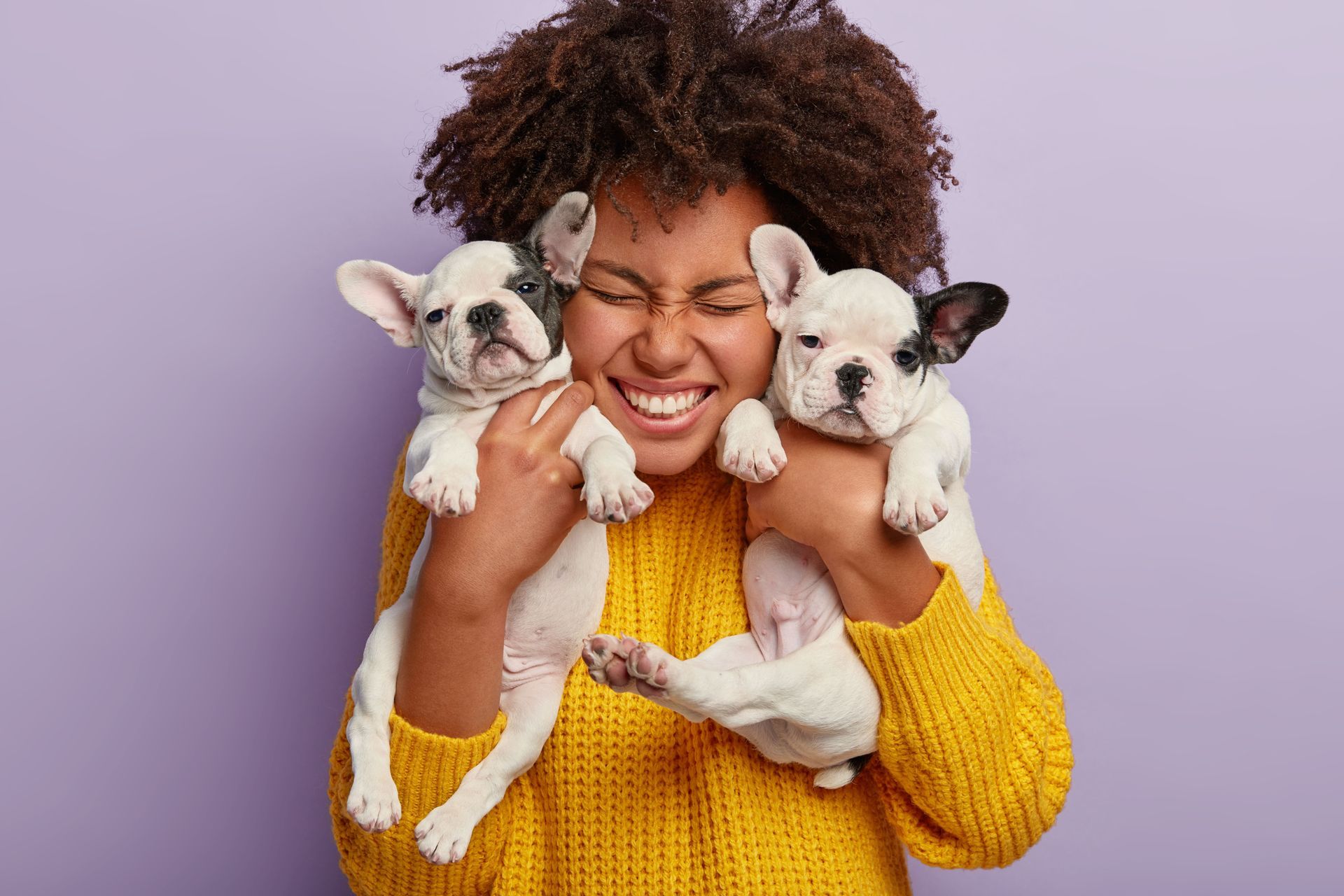 A woman in a yellow sweater is holding two puppies in her arms.
