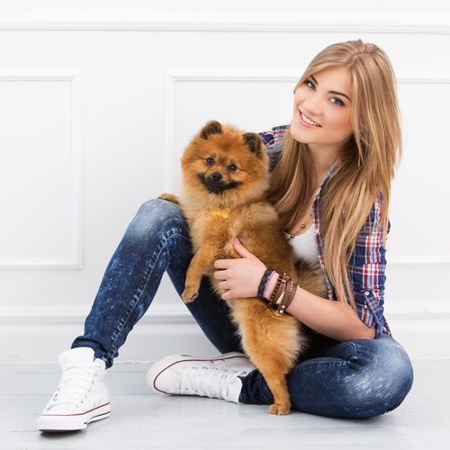 A woman is sitting on the floor holding a small dog.