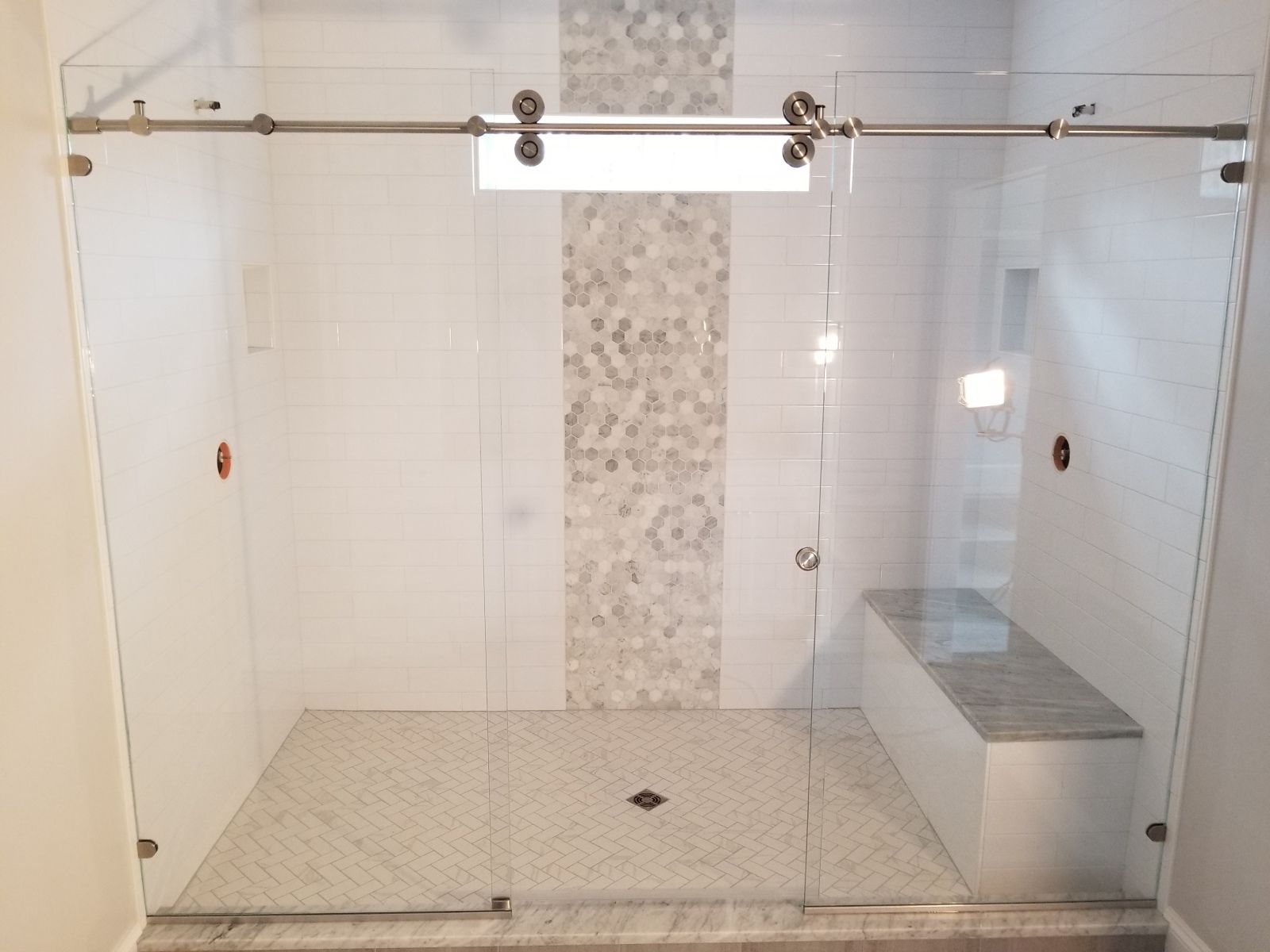 A bathroom with a sliding glass shower door and a bench.