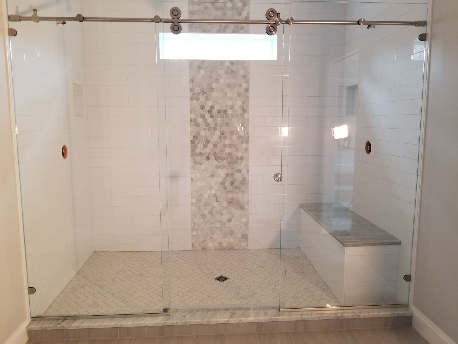 A bathroom with a sliding glass shower door and a bench.