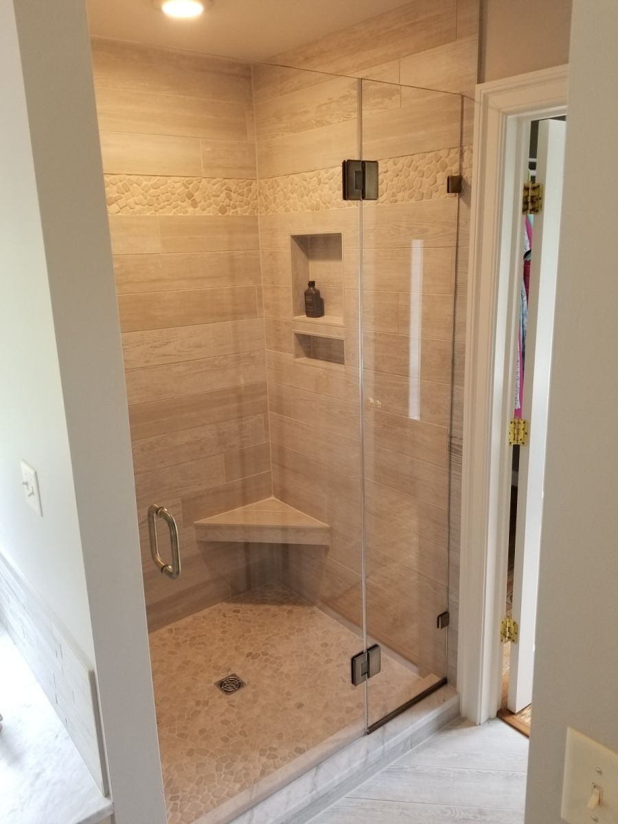 A bathroom with a glass shower door and a corner seat.