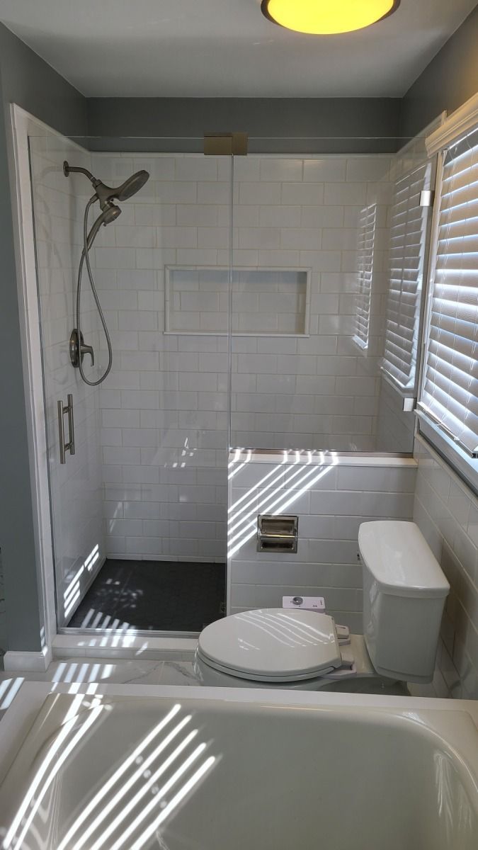 A bathroom with a tub , toilet , shower and window.