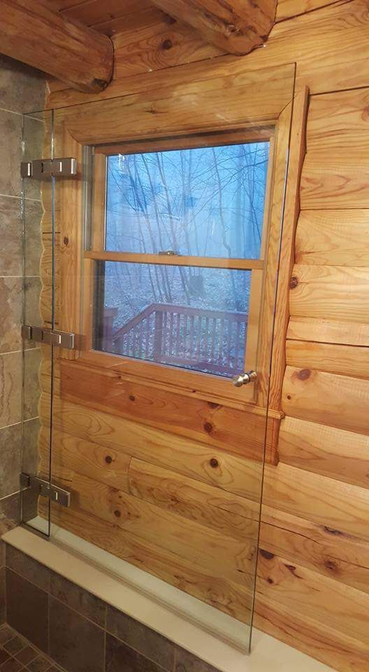 A bathroom in a log cabin with a glass shower door and a window.