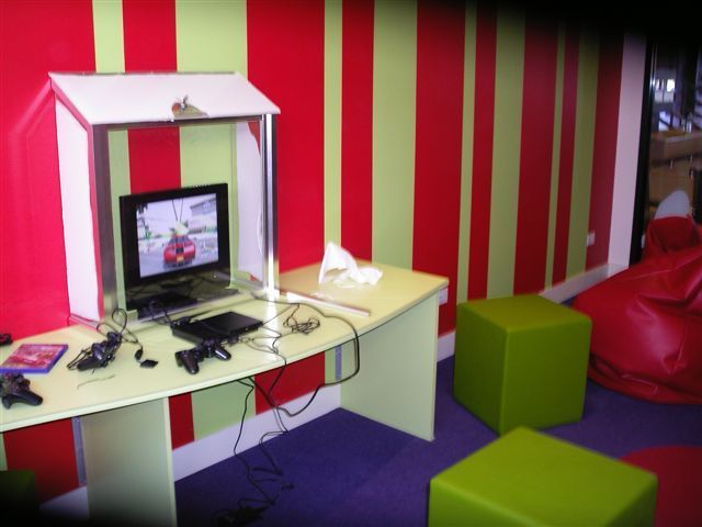 Small room with striped red walls, a computer desk, green stools, and a red beanbag chair.